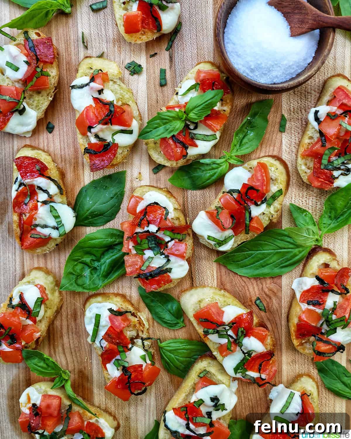 Delicious crostini pizzas arranged on a wooden board with a bowl of salt.