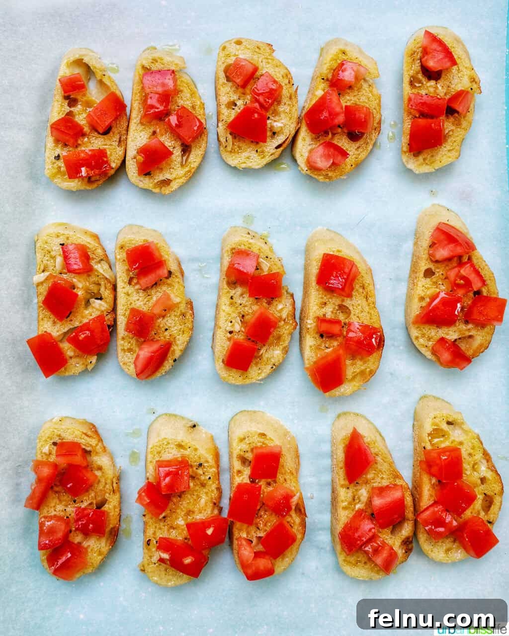 Sliced crostini on a baking sheet, topped with fresh tomatoes.
