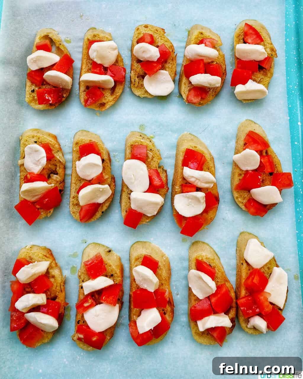 Sliced crostini on a baking sheet, topped with tomatoes and cheese.