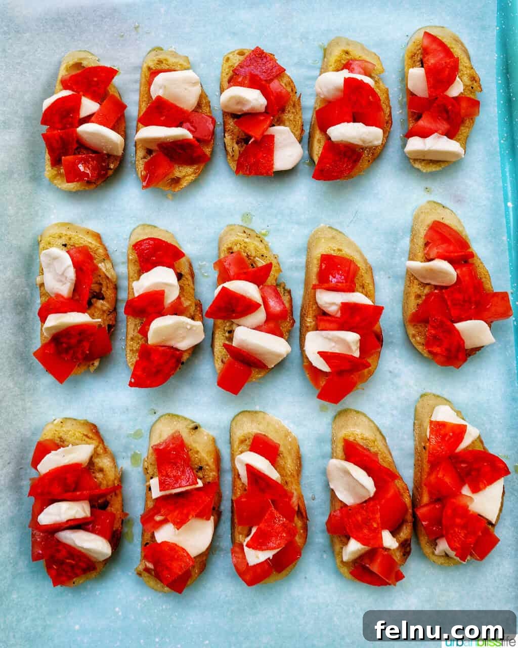 Sliced crostini on a baking sheet, topped with tomatoes, cheese, and pepperoni.