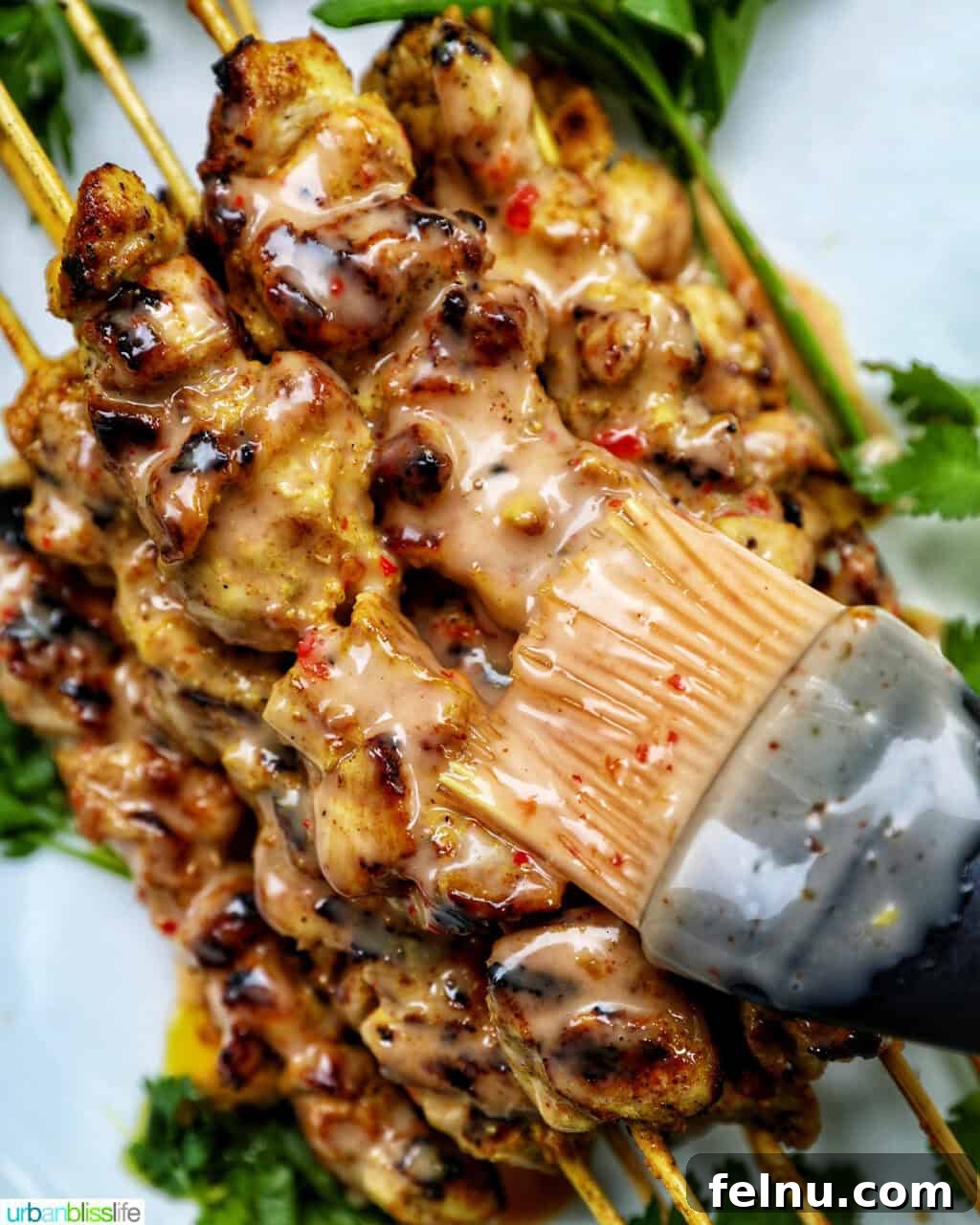 Spicy Peanut Glazed Chicken Skewers 12 A hand brushing the creamy Bang Bang sauce onto grilled chicken skewers.