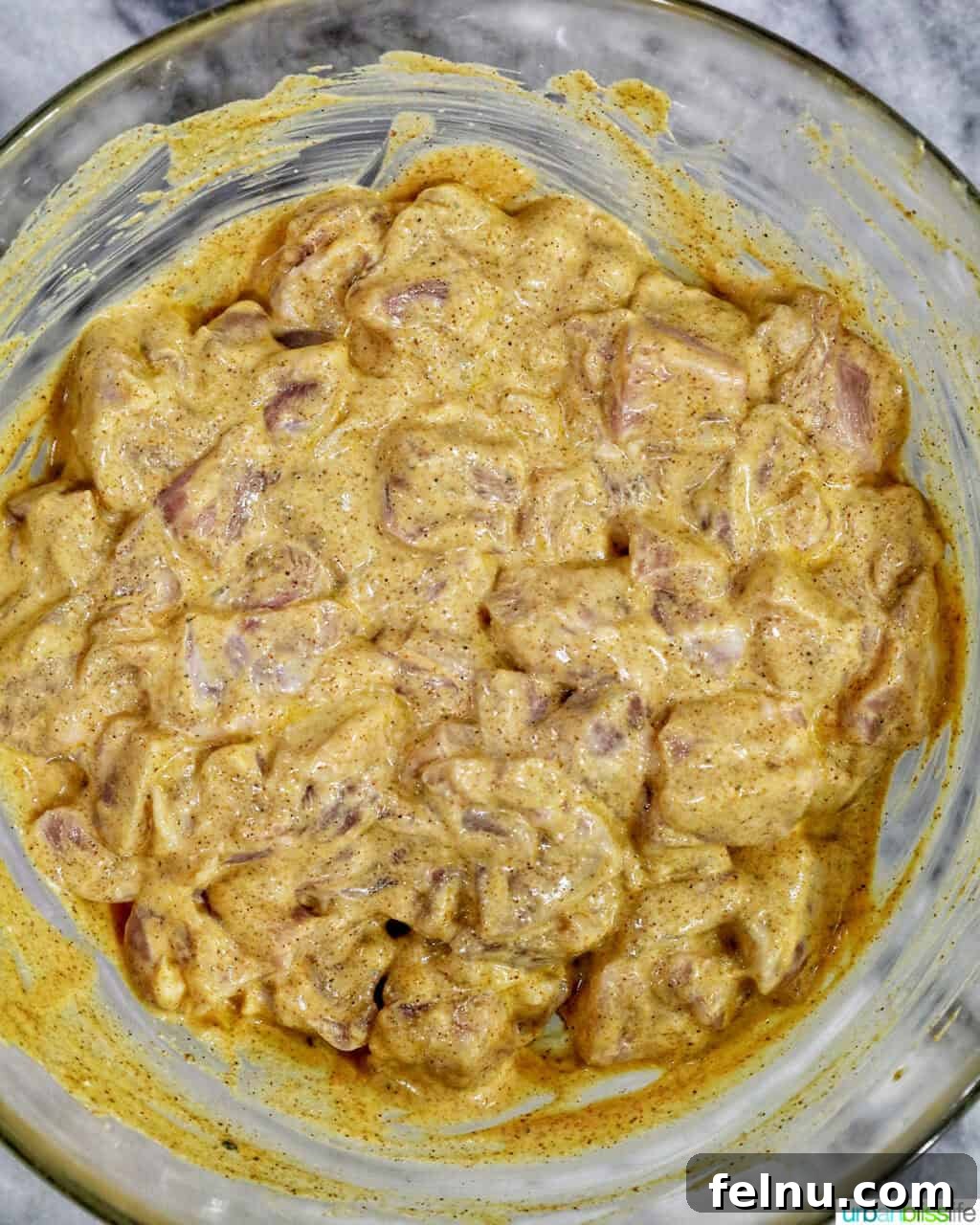 Spicy Peanut Glazed Chicken Skewers 6 Cubed chicken marinating in a creamy, spiced yogurt sauce within a glass bowl.