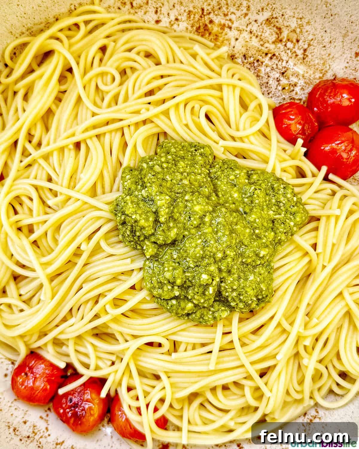 Vibrant Cherry Tomato Pesto Pasta 8 pesto added to spaghetti pasta with cherry tomatoes in a pan.