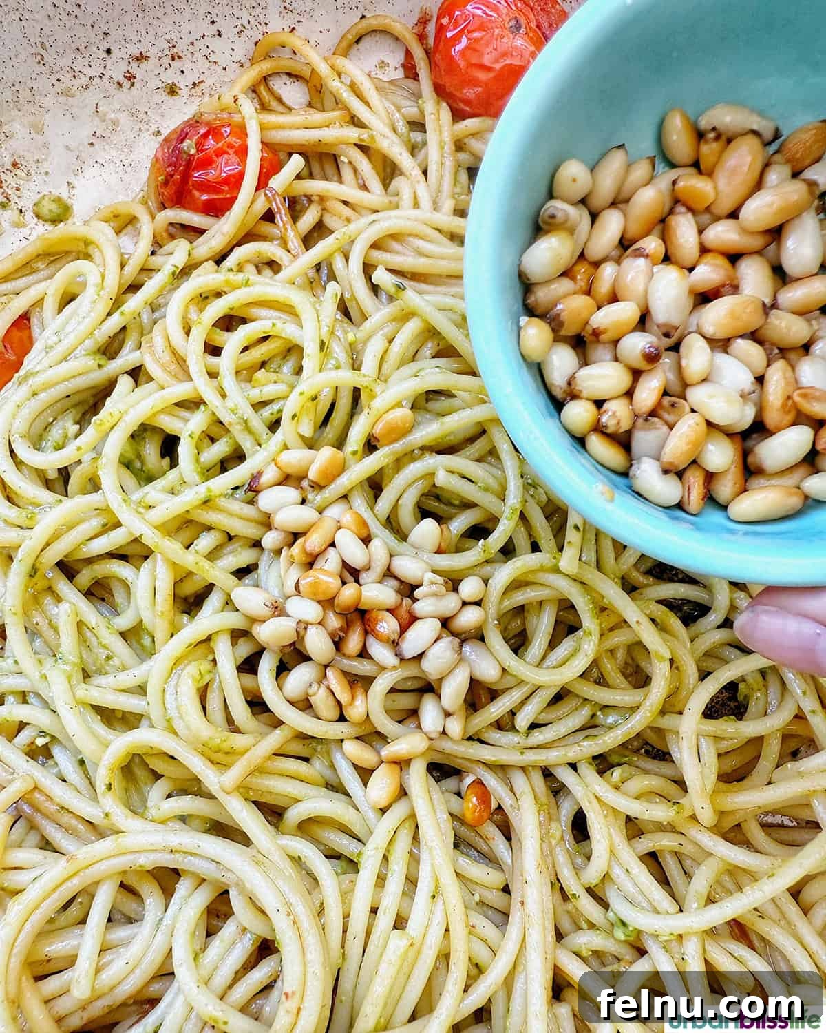 Vibrant Cherry Tomato Pesto Pasta 9 pine nuts added to pesto and spaghetti pasta with cherry tomatoes in a pan.
