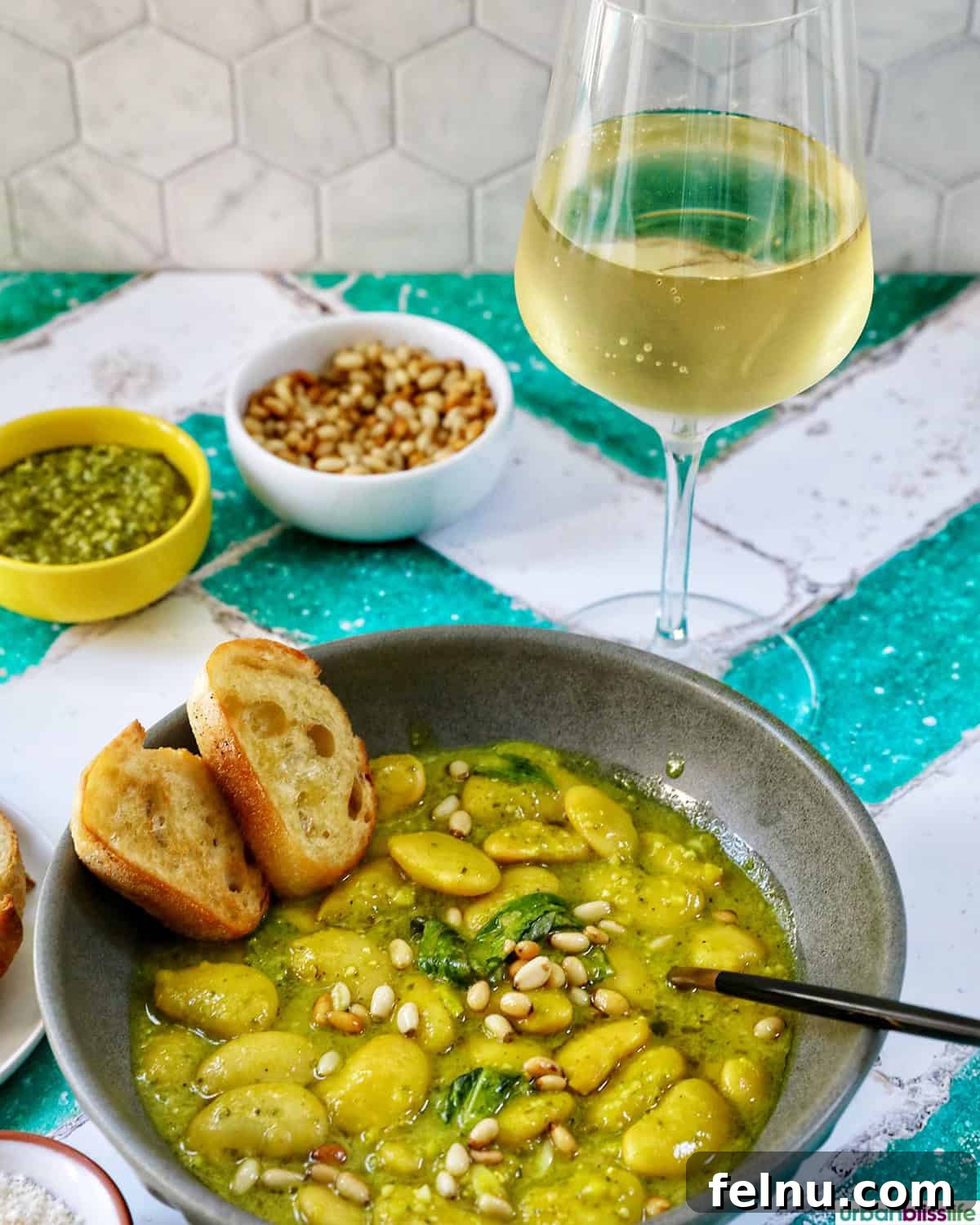 bowl of pesto beans with crostini slices and side bowls of parmesan cheese and pine nuts and a glass of white wine.