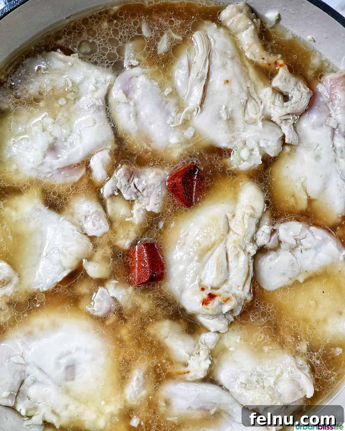 Rich Filipino Peanut Chicken 11 Chicken simmering in a rich, reddish-brown sauce in a pan.