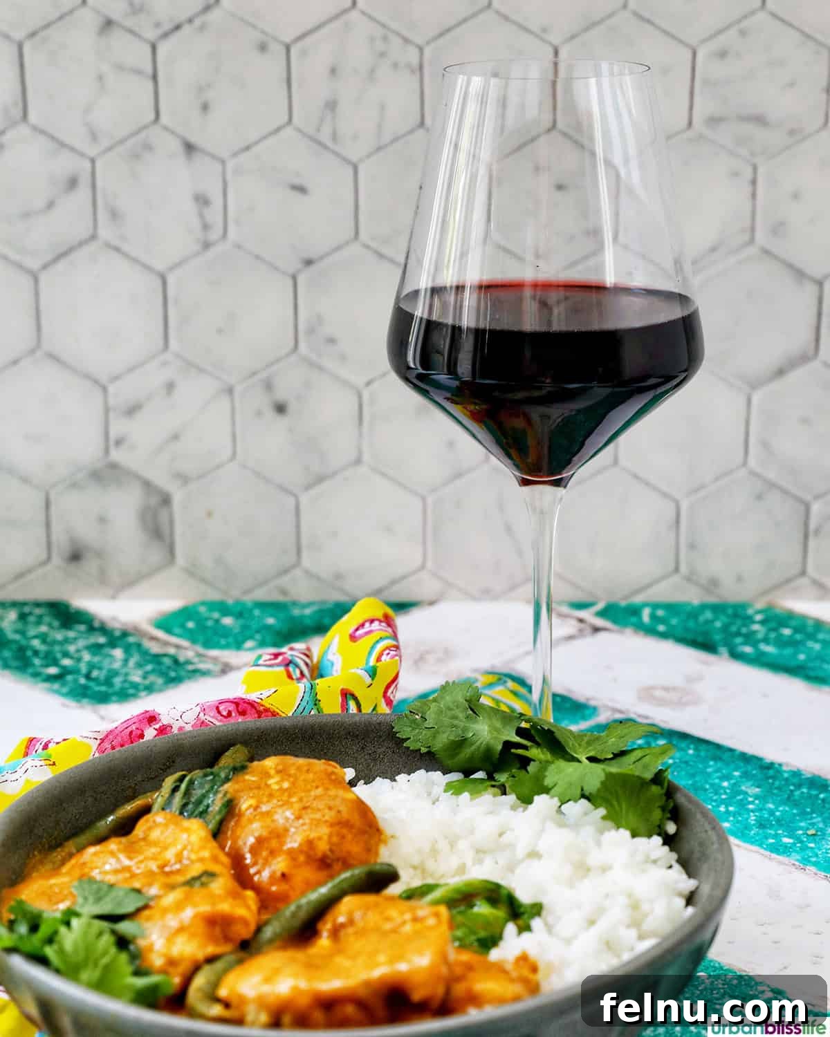 Rich Filipino Peanut Chicken 19 A glass of red wine next to a plate of chicken kare kare and rice, ready for a meal.