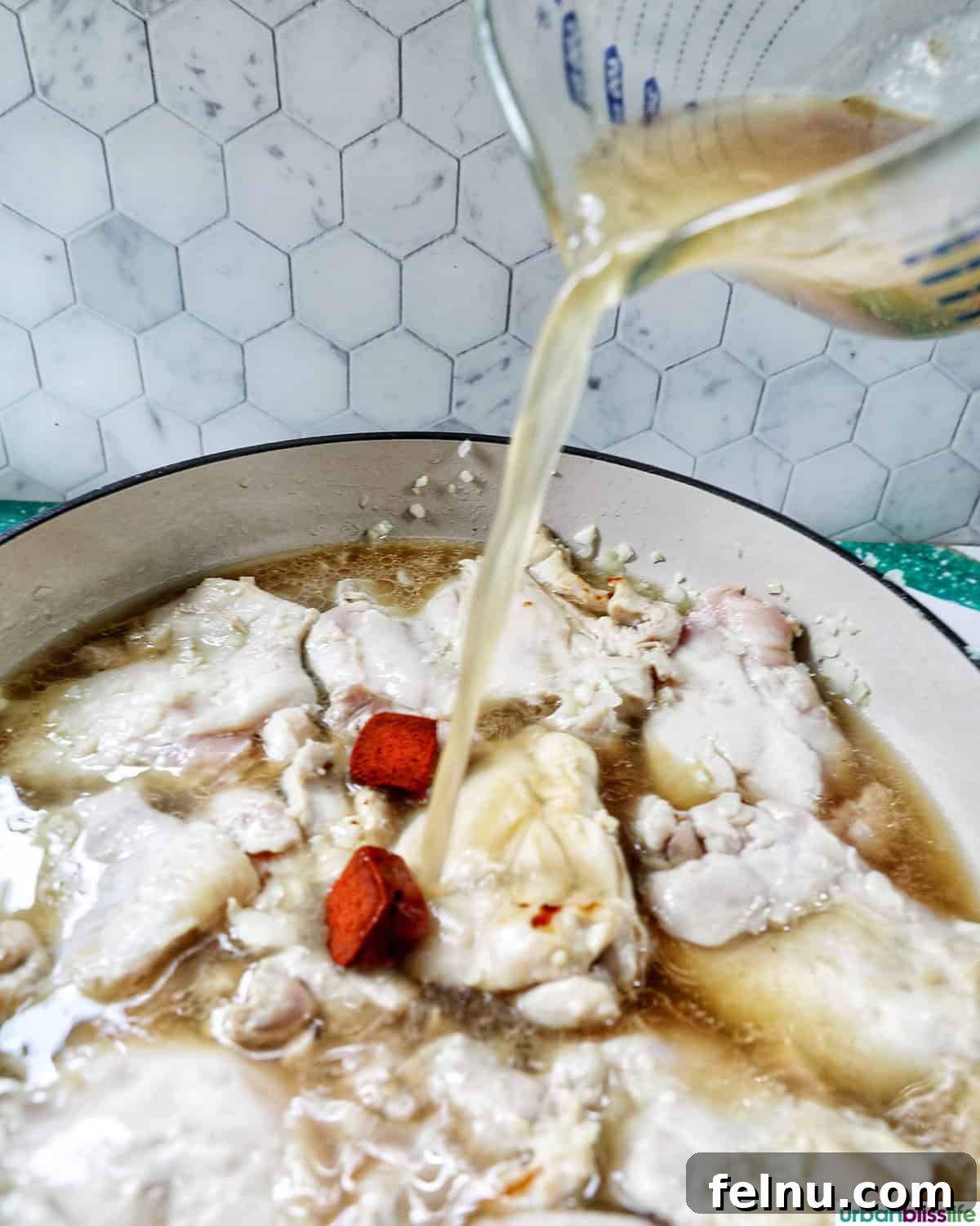 Rich Filipino Peanut Chicken 10 Chicken broth being poured over browned chicken in a pan.