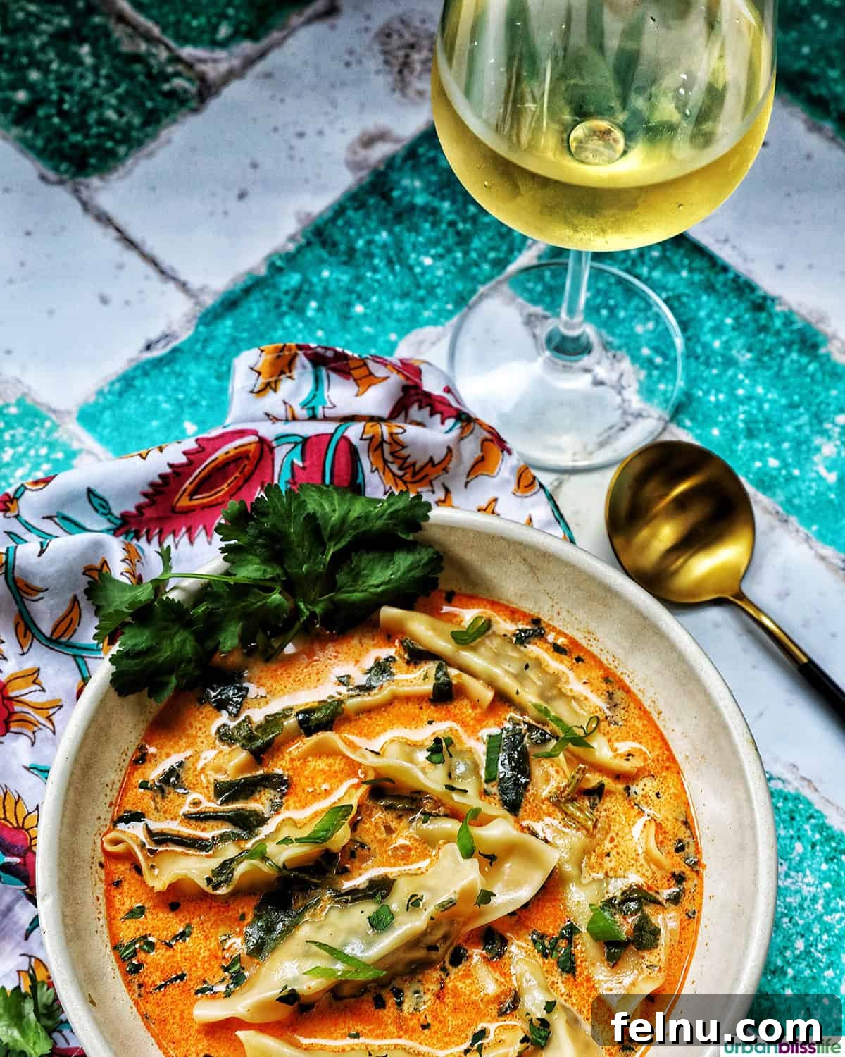 Aromatic Thai Red Curry Dumpling Soup 13 A bowl of Thai red curry dumpling soup, accompanied by a spoon and a glass of wine.