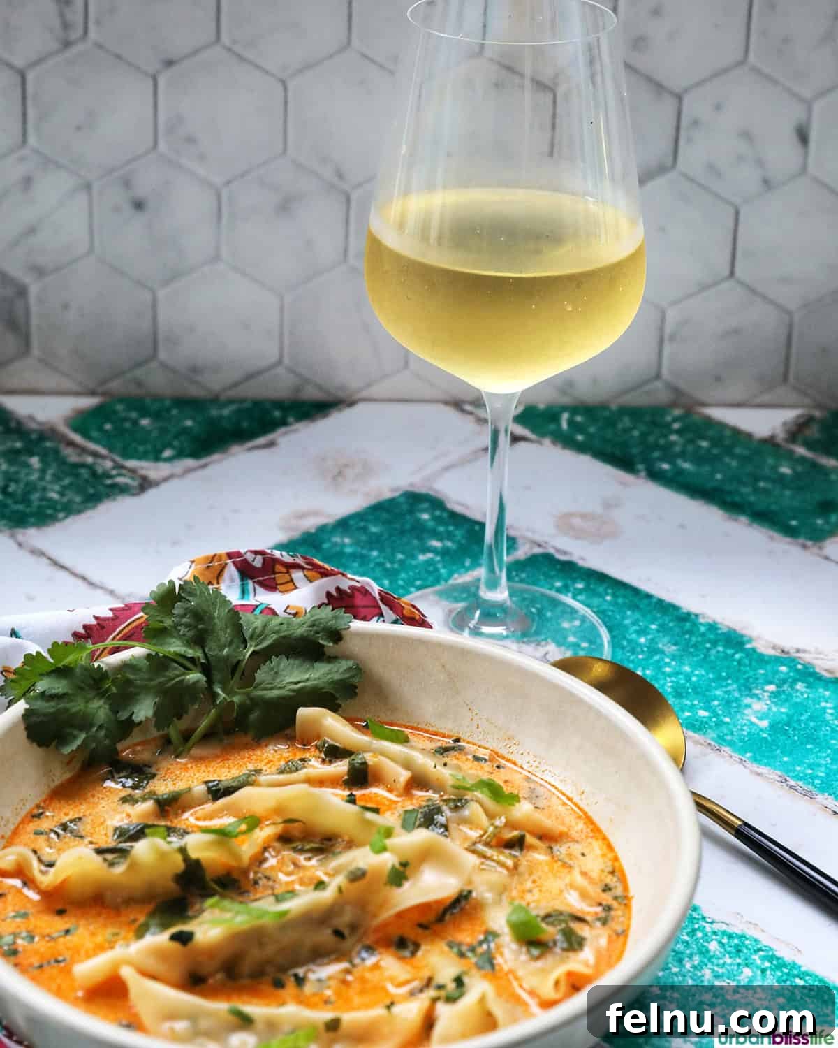 Aromatic Thai Red Curry Dumpling Soup 14 A bowl of Thai red curry dumpling soup, with a spoon resting in it and a glass of wine beside it.