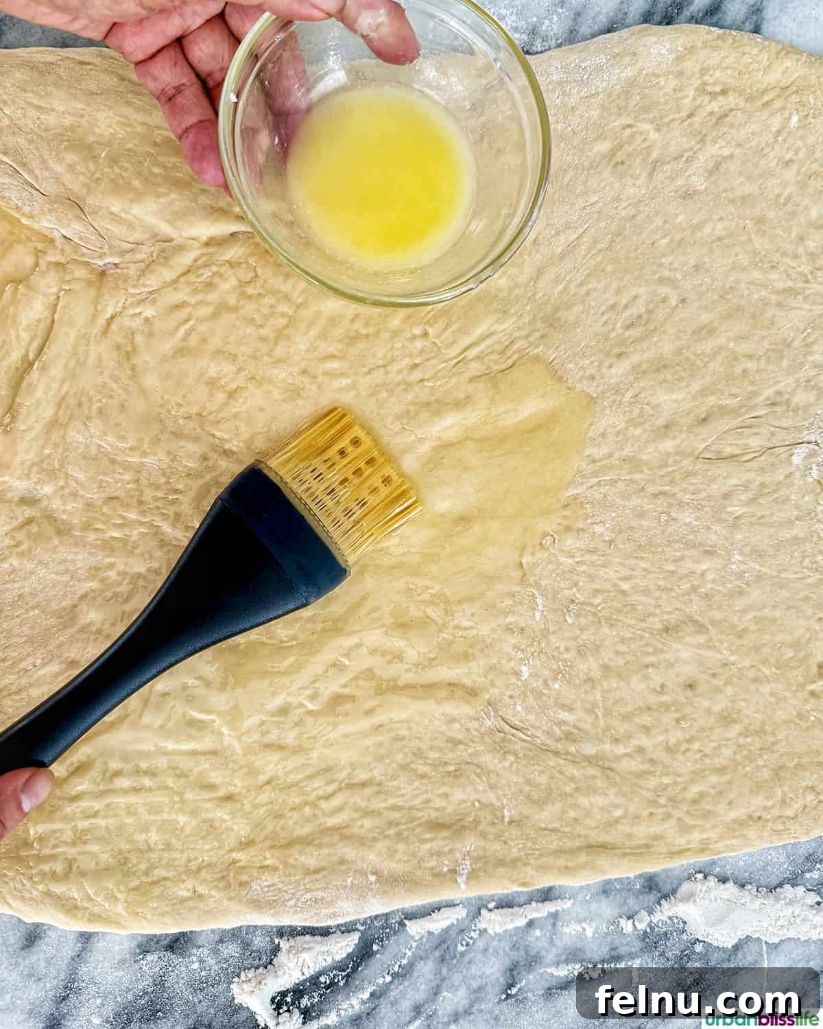 Pastry brush applying melted butter onto the rolled-out dough.