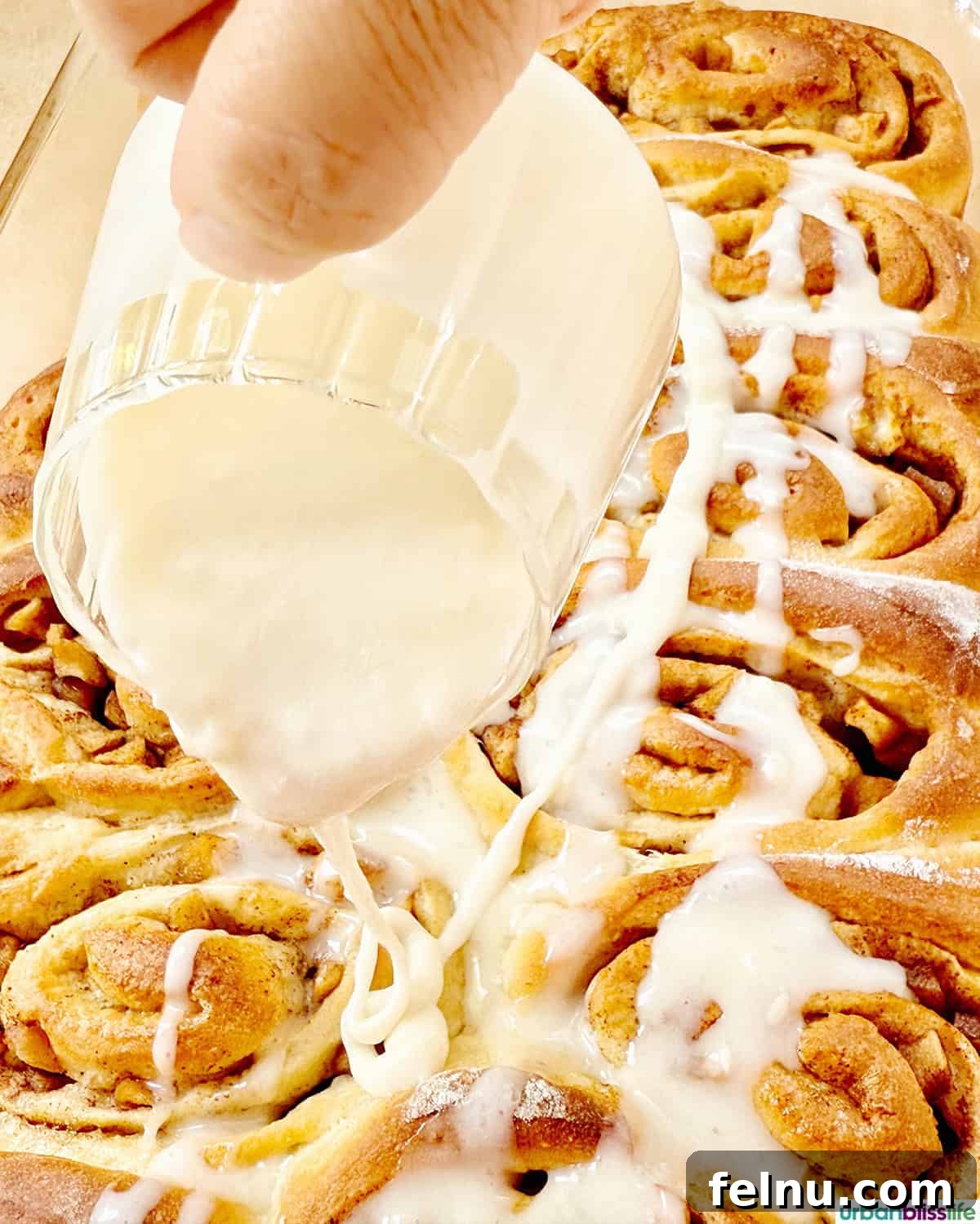 Pouring creamy icing over warm apple pie cinnamon rolls.