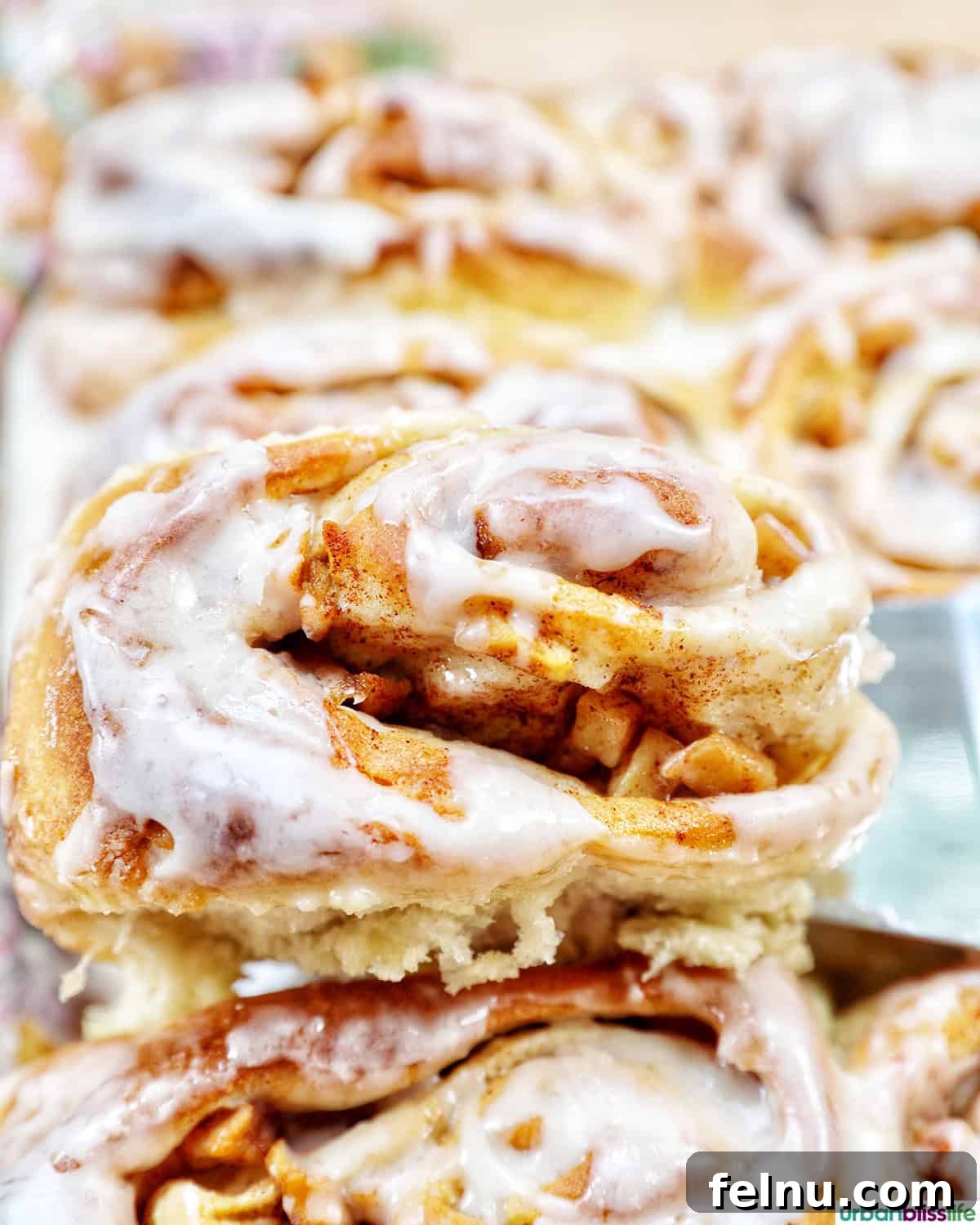 Freshly baked apple pie cinnamon rolls being lifted from a pan.