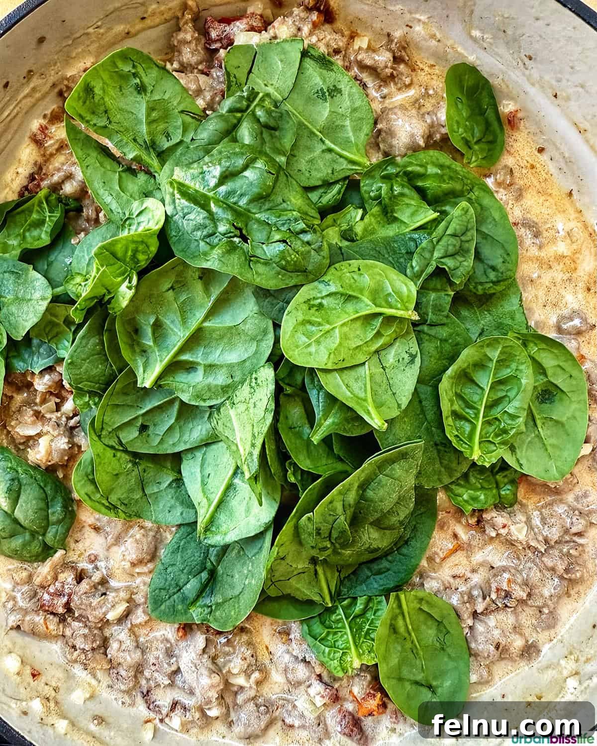 Tuscan Sausage Pasta Delight 16 Spinach on top of sausage sauce in a pan