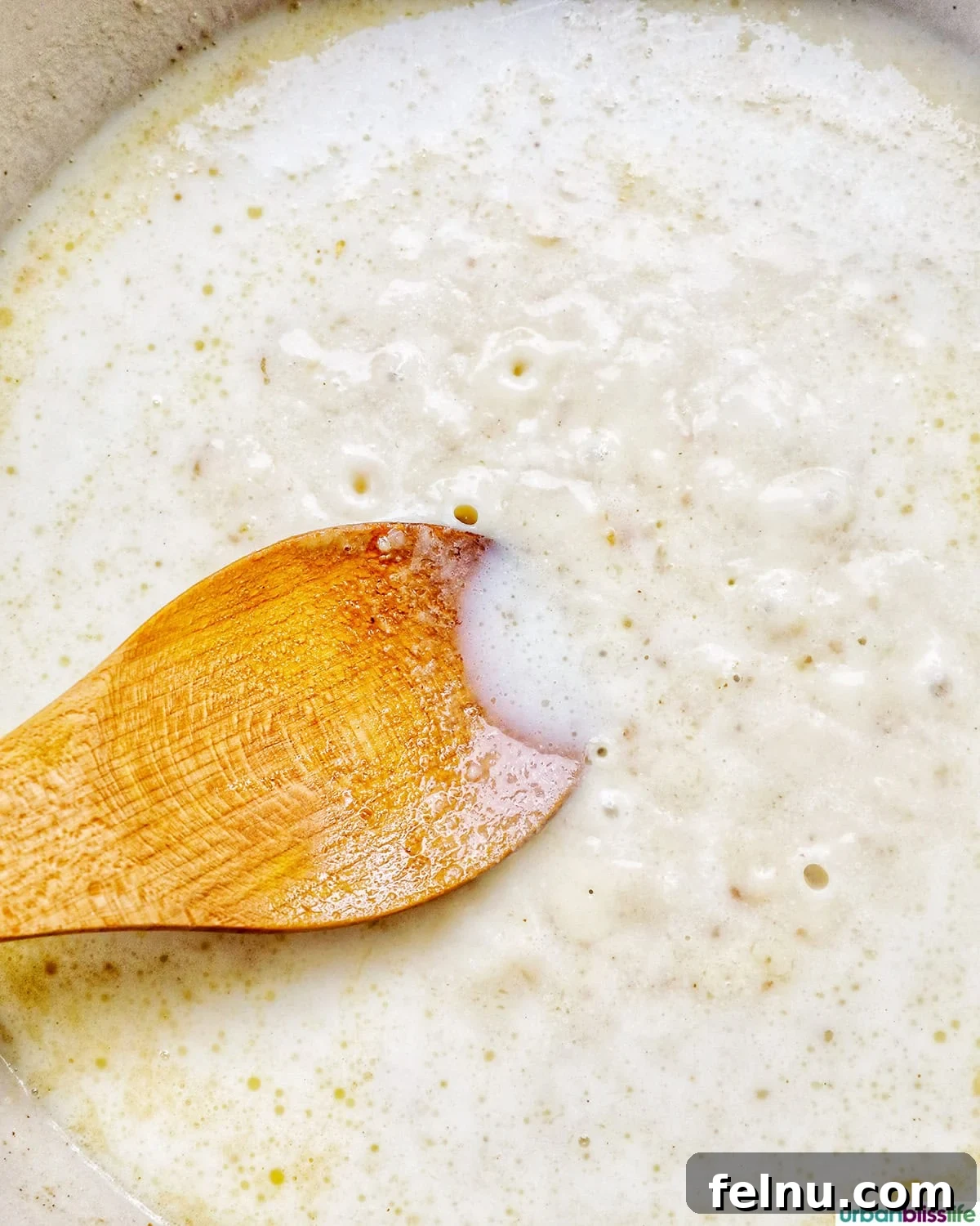 A wooden spoon stirring a smooth, bubbling roux, a creamy base for the cheese sauce.