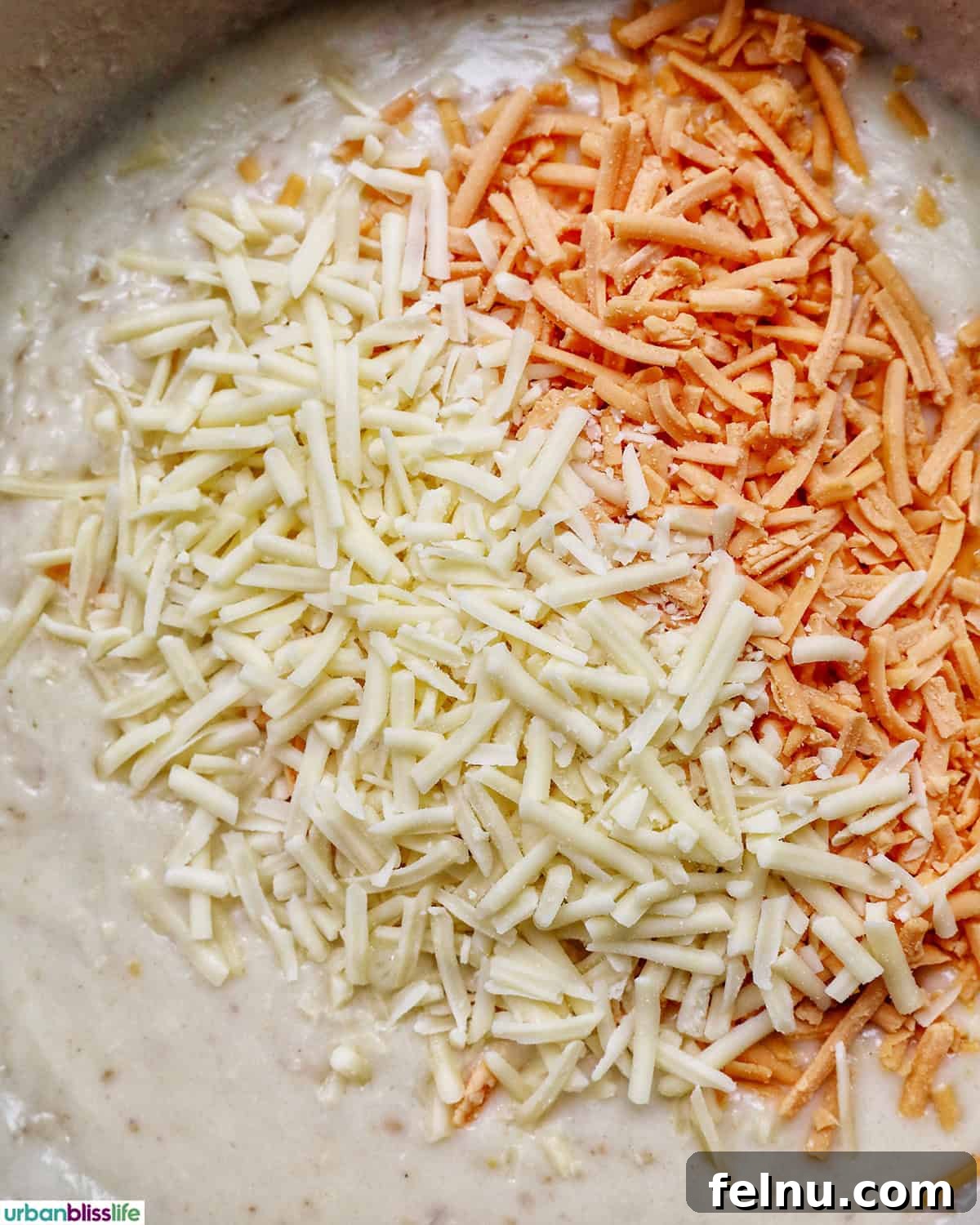 A generous amount of shredded cheeses starting to melt into the creamy white sauce in a pan.