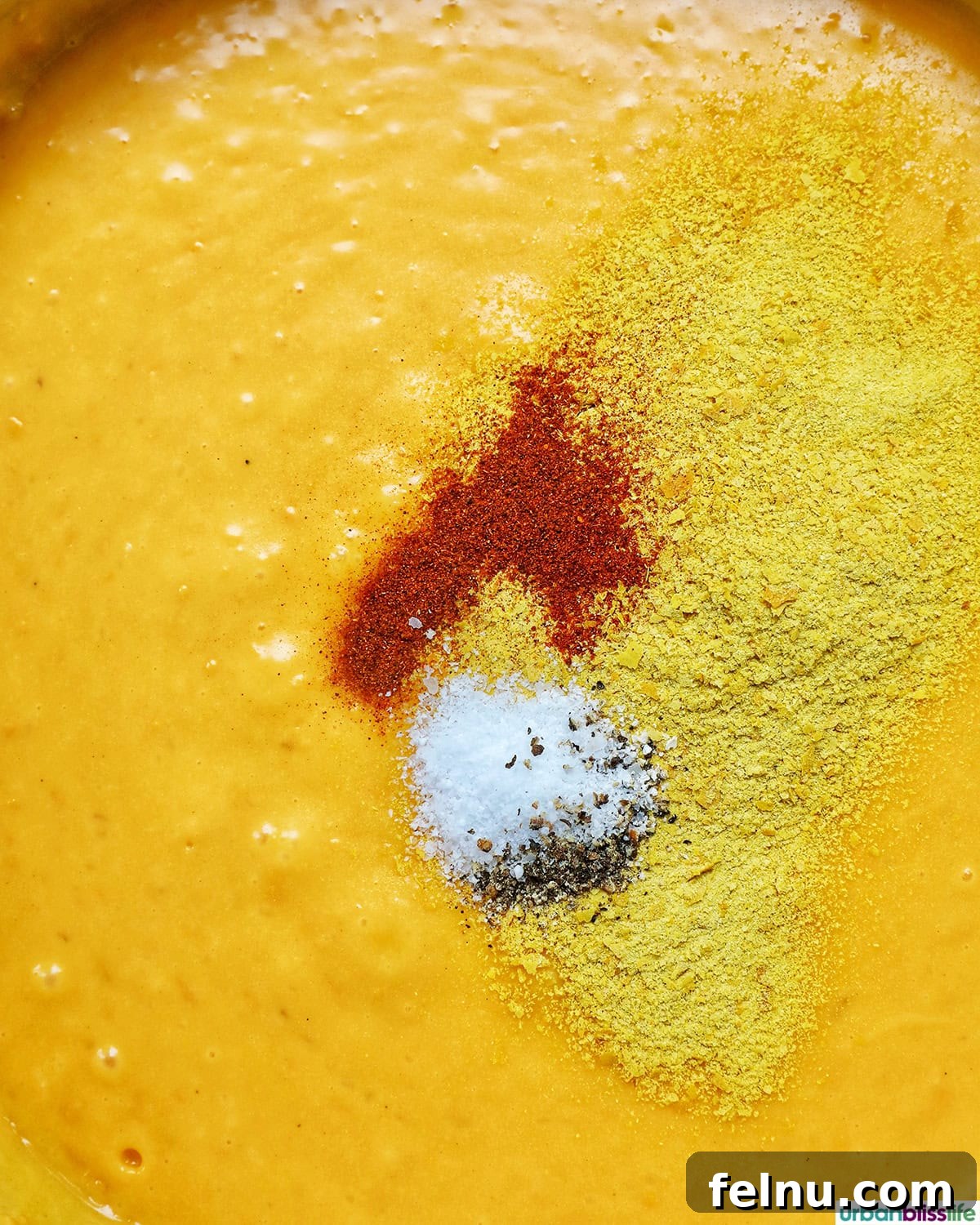 A medley of spices, including nutritional yeast, salt, pepper, and paprika, mixed into the rich cheese sauce.