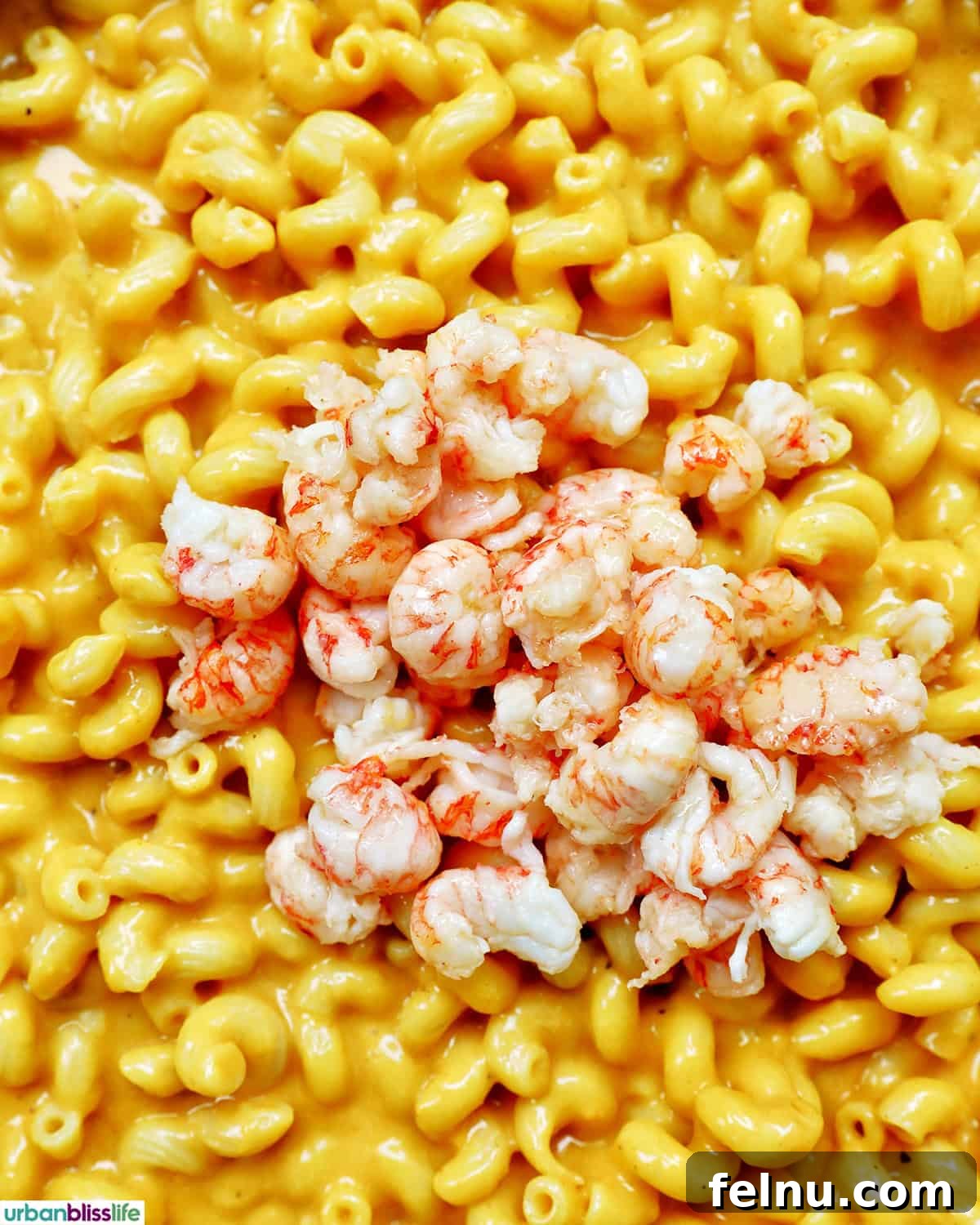 Succulent chunks of cooked lobster being folded into the creamy dairy-free mac and cheese, creating a harmonious blend.