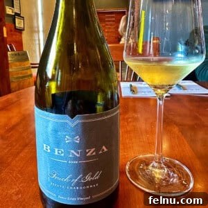 A close-up of a wine glass and a bottle of white wine, with a blurred background suggesting a vineyard or winery.