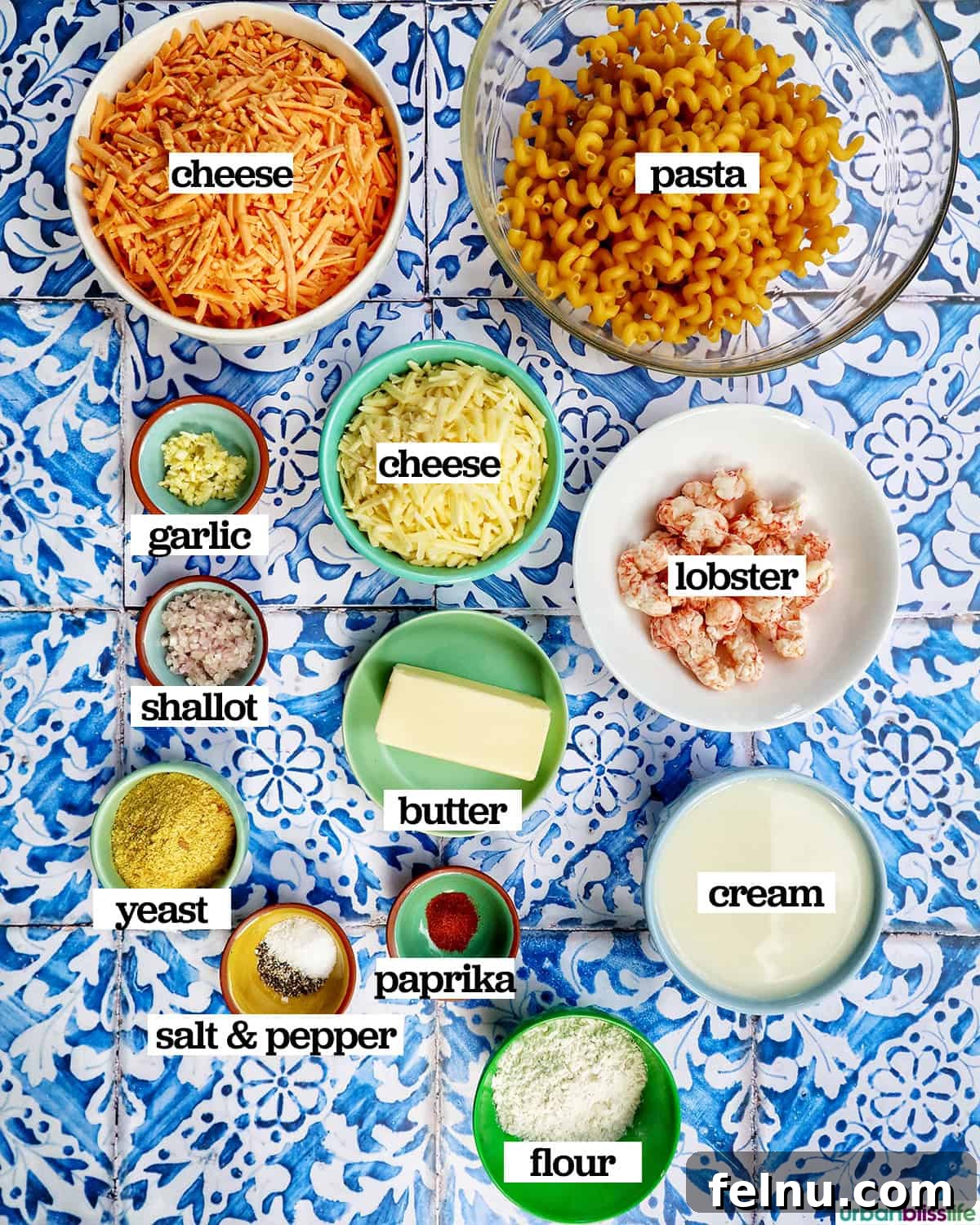 Various bowls holding fresh ingredients for lobster mac and cheese, including pasta, lobster meat, shredded cheese, and aromatics.