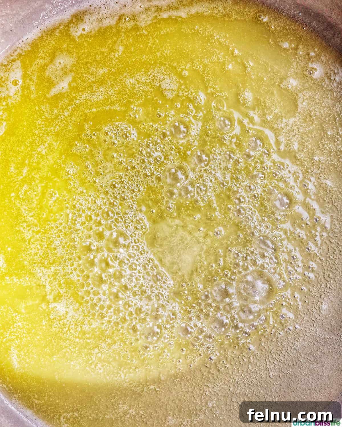 Vegan butter gently melting in a pan over medium heat, forming a shimmering liquid.