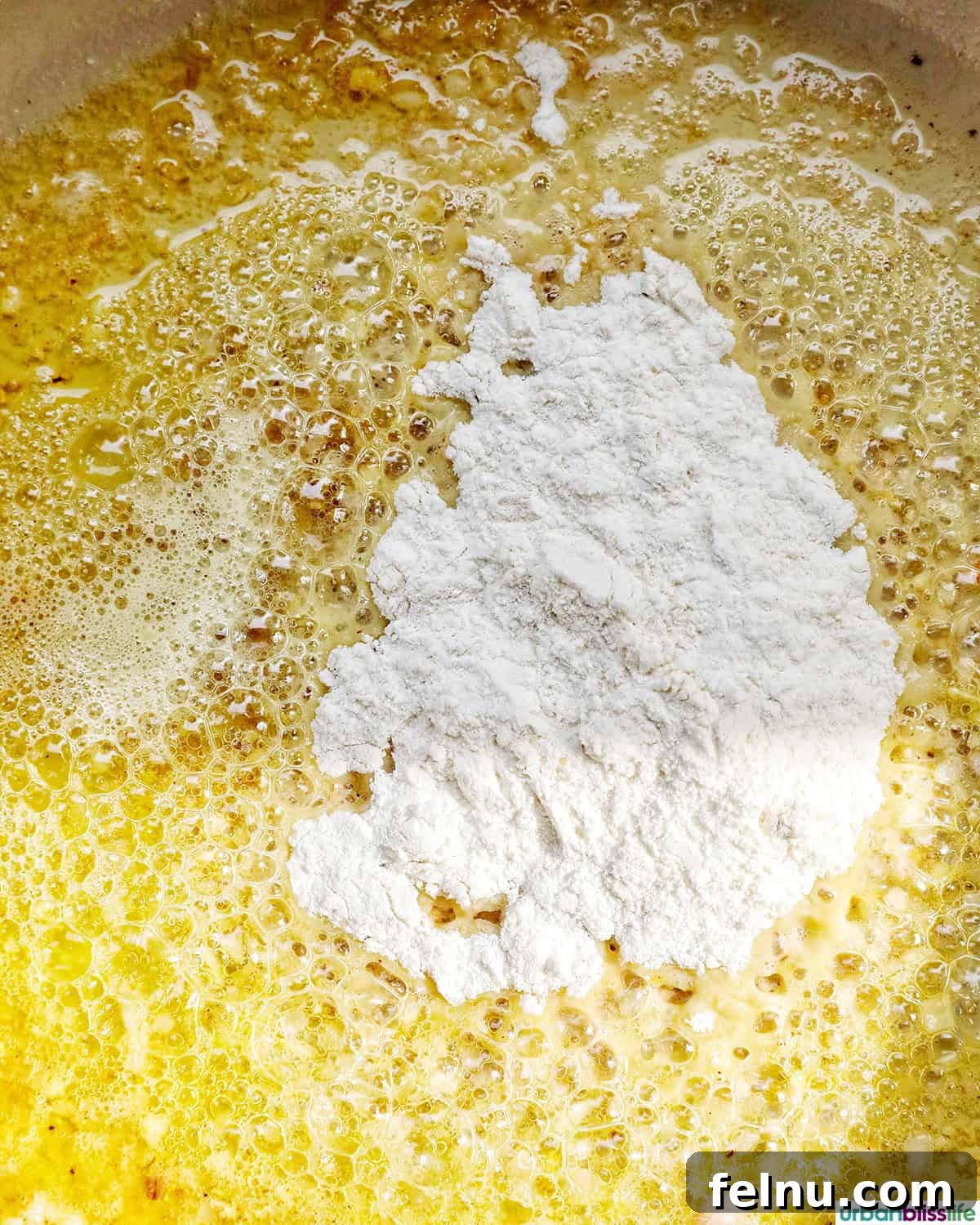 Flour being whisked into the butter and aromatics in a pan, starting to form a roux.
