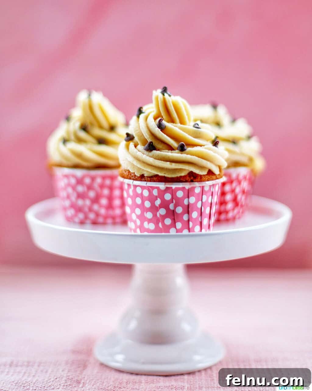 Chocolate Chip Cookie Dough Dream Cupcakes 2 Three Chocolate Chip Cupcakes with Cookie Dough Frosting on a white cake pedestal with pink background