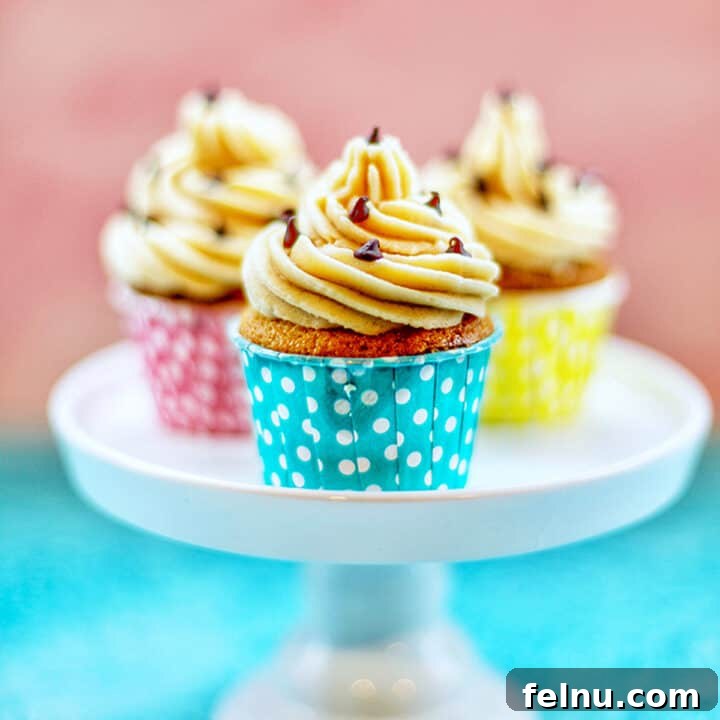 chocolate chip cupcakes with cookie dough frosting in blue, pink, and yellow cups on a pedestal.