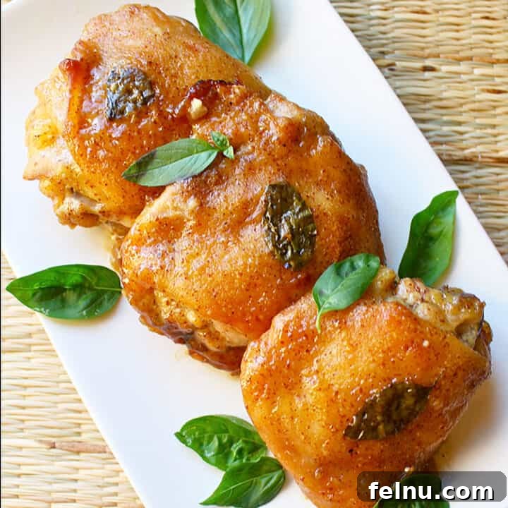 Three honey mustard chicken thighs with basil leaves on a white plate.