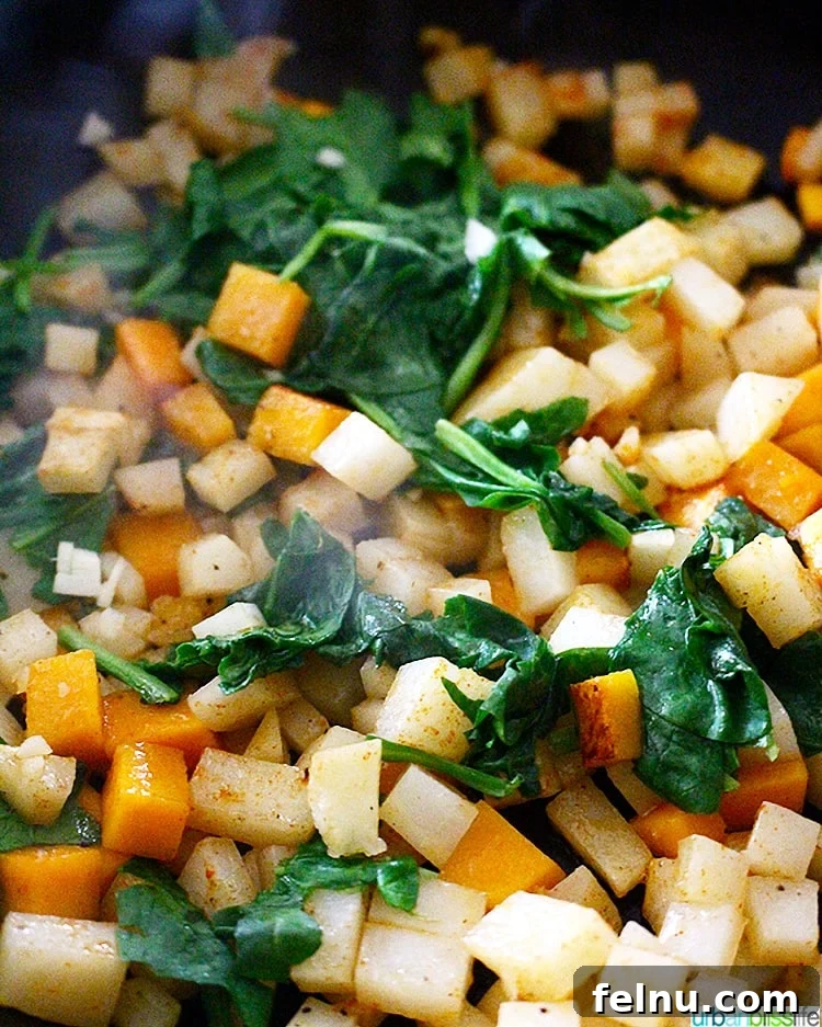 Butternut squash hash cooking in a pan with fresh spinach, showing the vibrant ingredients combining