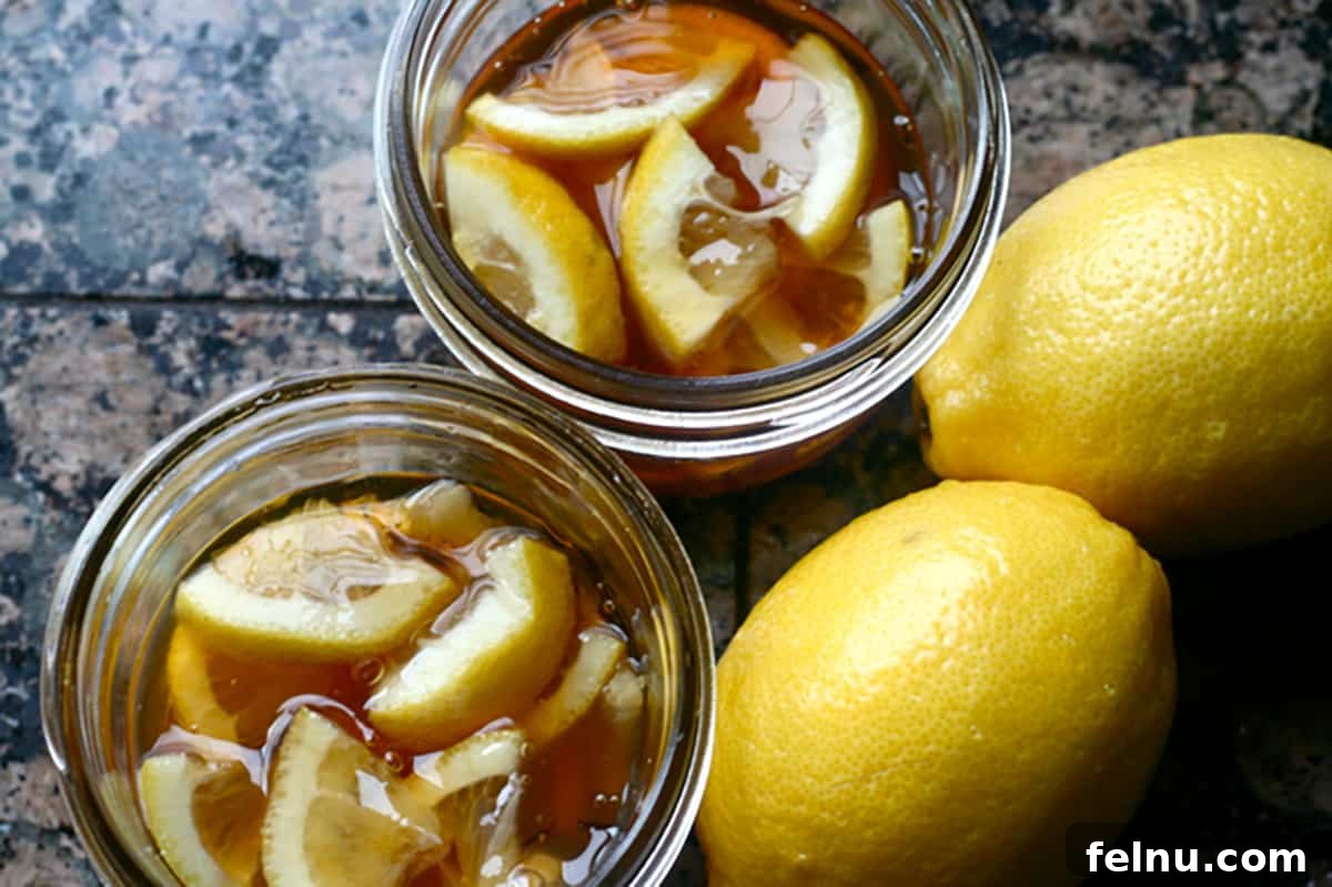 Two mason jars of ginger lemon and honey syrup, with two lemons on the side