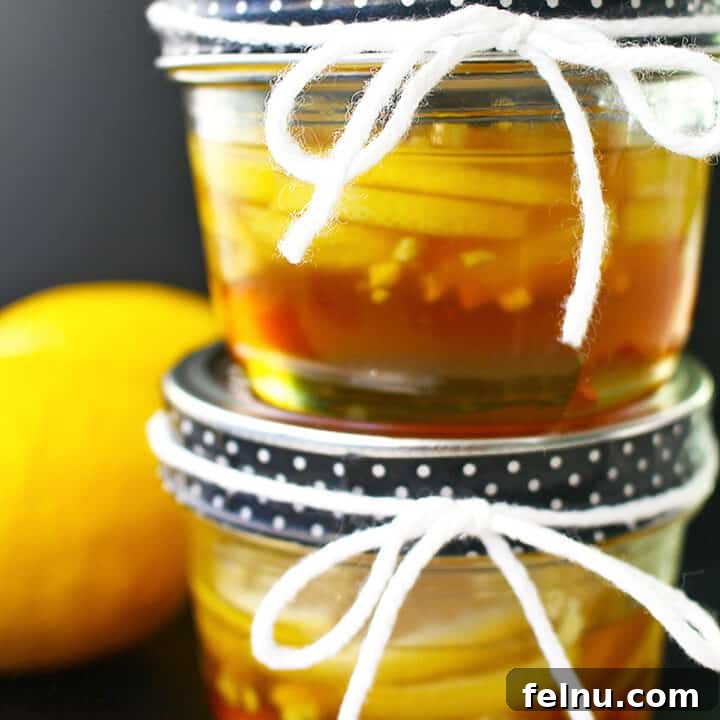 two mason jars of ginger lemon and honey marmalade stacked, with a lemon on the side.