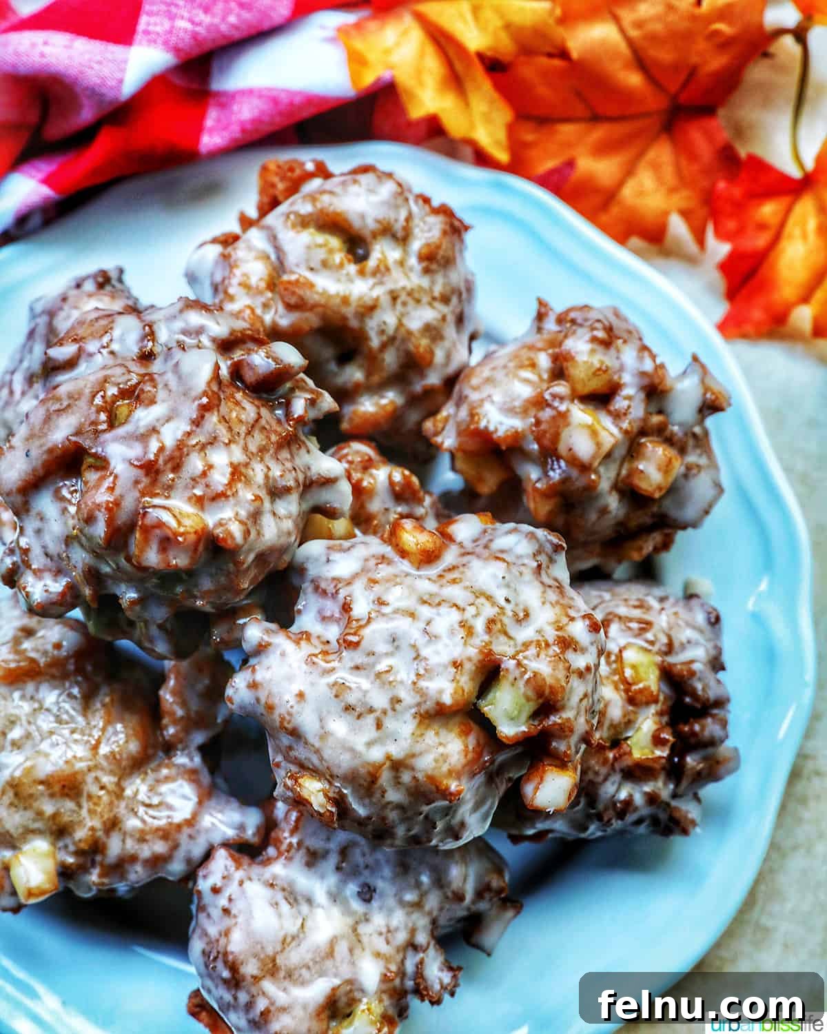 Crispy Cinnamon Apple Fritters 2 Freshly made apple fritter donuts stacked on a plate, gleaming with cinnamon glaze.