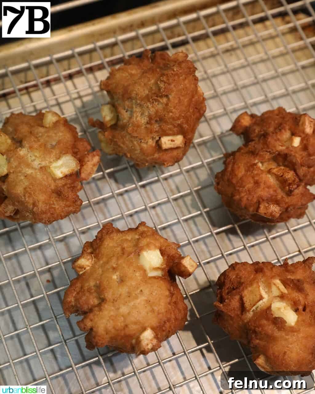 Crispy Cinnamon Apple Fritters 15 Hot apple fritter donuts draining on a wire rack.