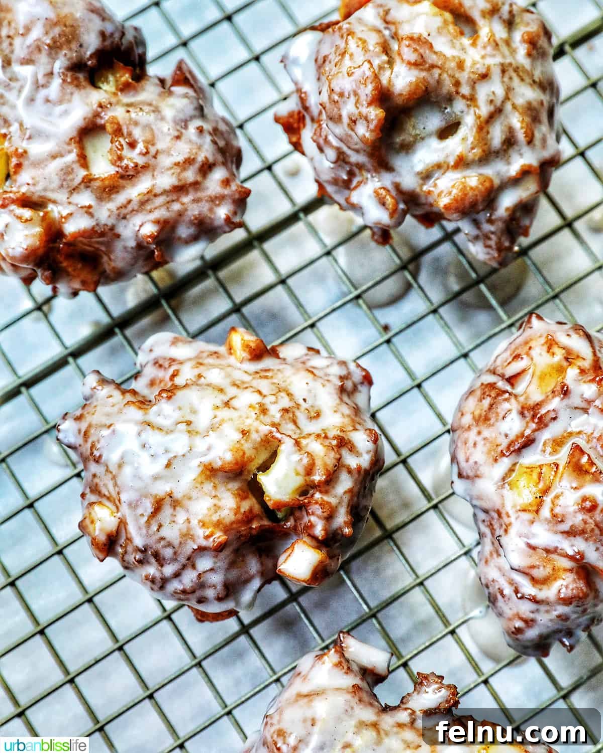 Crispy Cinnamon Apple Fritters 18 Close-up of a glazed apple fritter donut on a wire rack, showing its crispy texture.
