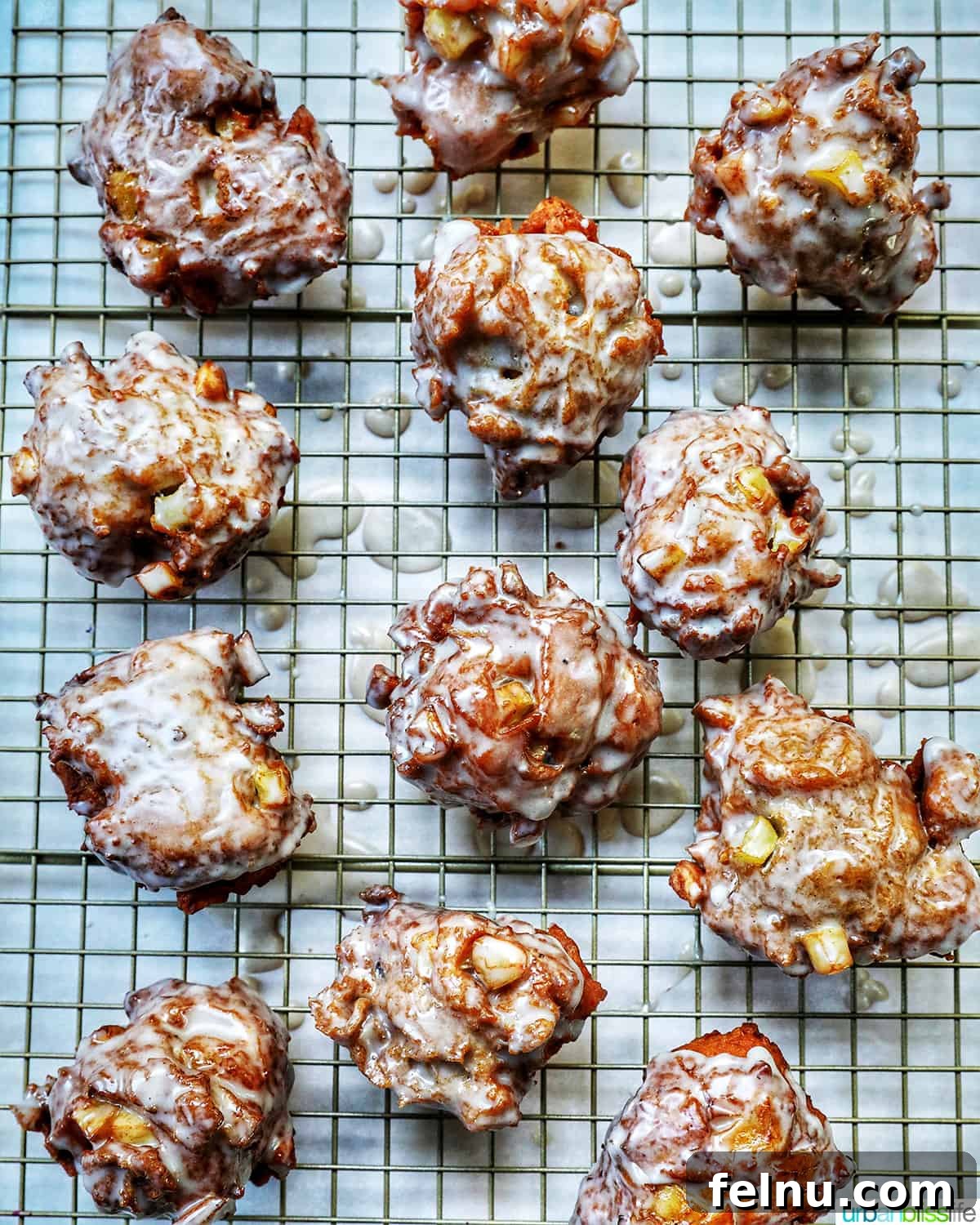 Crispy Cinnamon Apple Fritters 3 Glazed apple fritter donuts cooling on a wire rack, ready to be enjoyed.