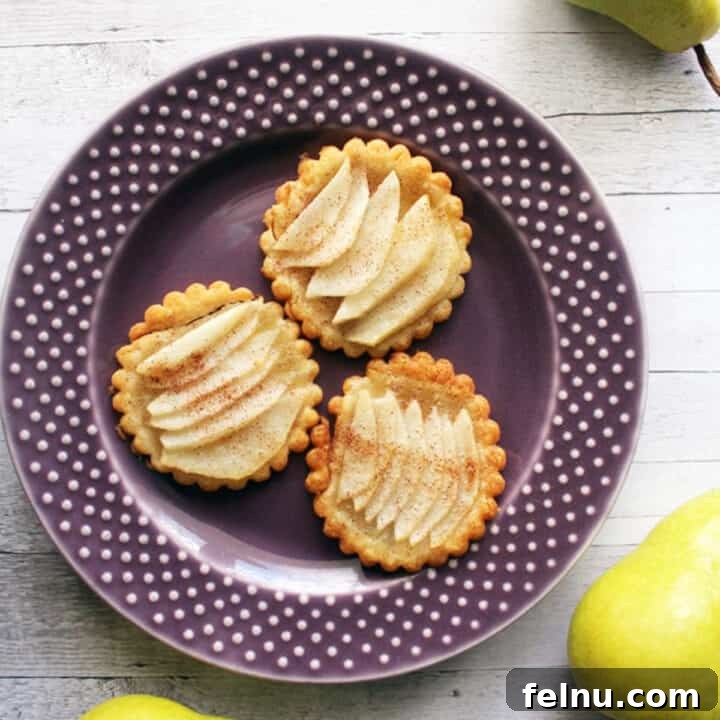Three perfectly baked pear tartlets arranged on a vibrant purple plate, each showcasing a golden crust and tender, caramelized pear slices. An inviting autumn dessert.