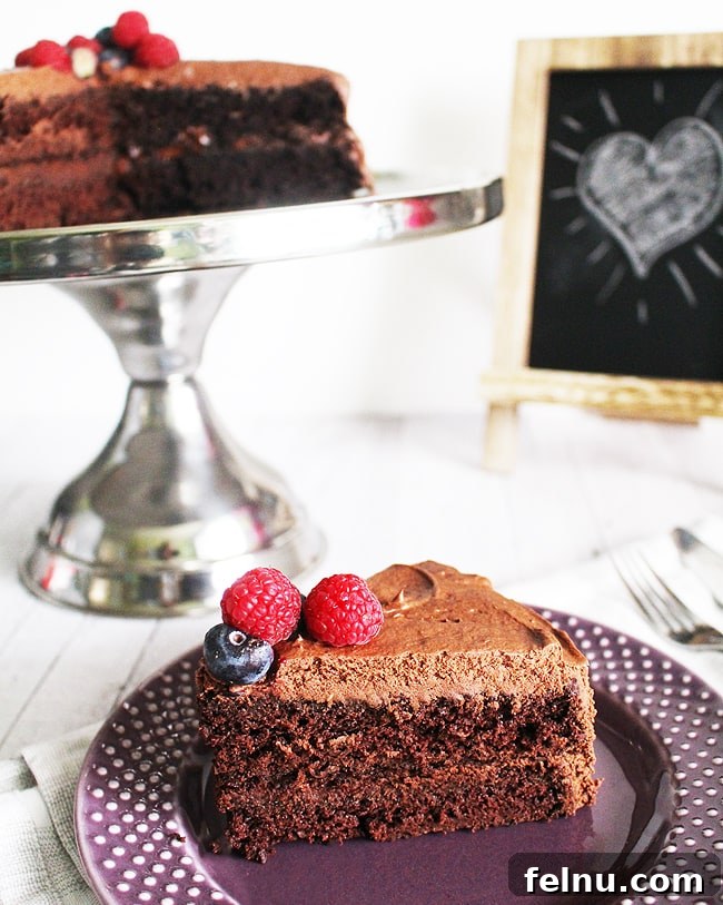 Close-up of a slice of vegan chocolate cake with the full cake in the background.