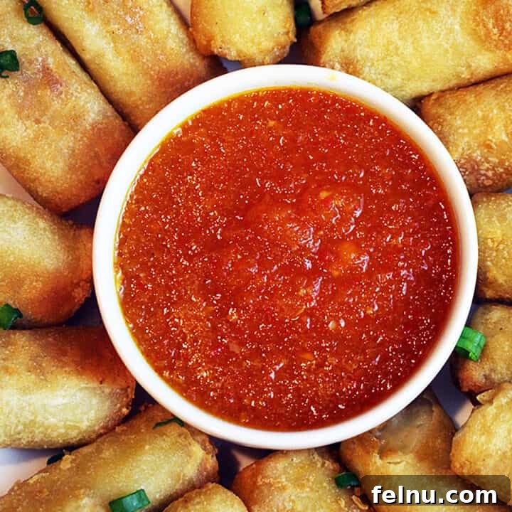 Sweet chili dipping sauce in a bowl surrounded by egg rolls.