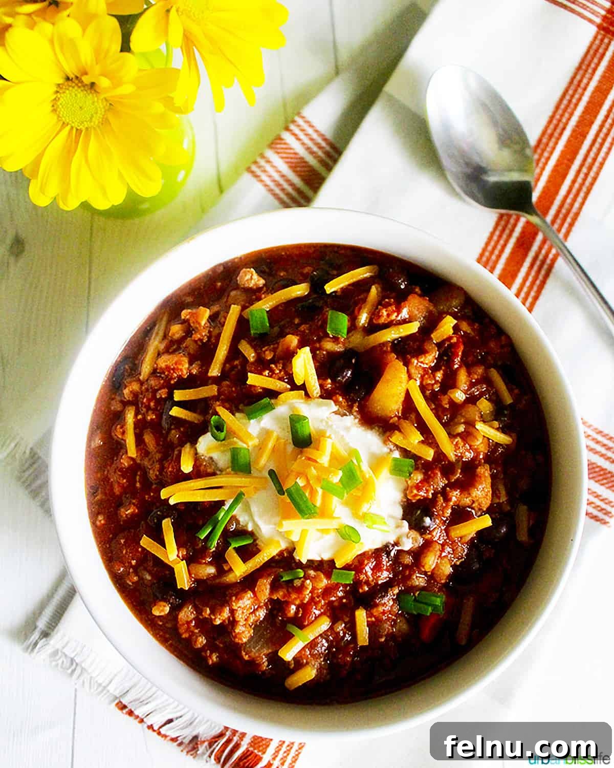Hearty Dutch Oven Turkey Chili with Farro and Stout 2 A steaming bowl of hearty Dutch oven turkey chili topped with fresh herbs, alongside a vase of cheerful yellow daisies, highlighting its comforting appeal.