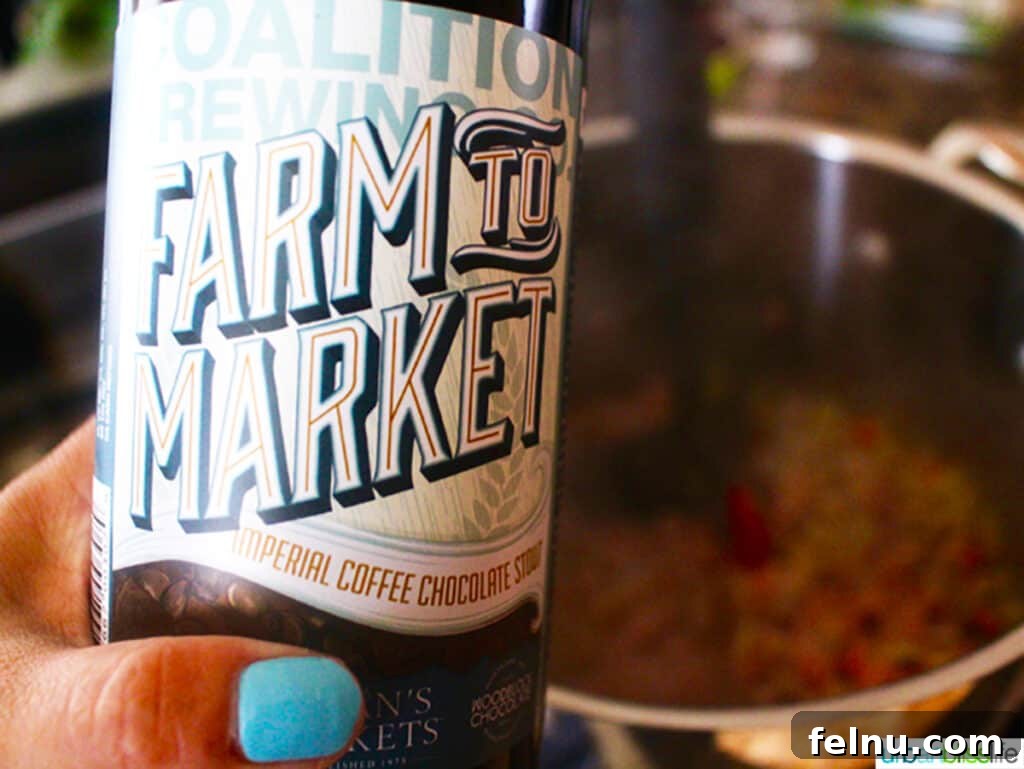 Hearty Dutch Oven Turkey Chili with Farro and Stout 4 A hand holding a frosty glass of dark coffee stout beer, symbolizing the rich, deep flavor it adds to the chili.