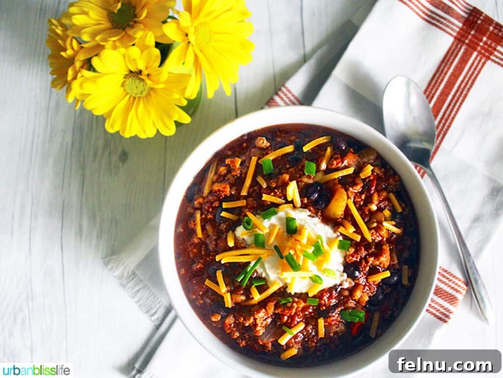 Hearty Dutch Oven Turkey Chili with Farro and Stout 6 A generously filled bowl of hearty Dutch oven turkey chili, artfully garnished with various toppings like cheese, sour cream, and green onions, positioned for a cozy meal.
