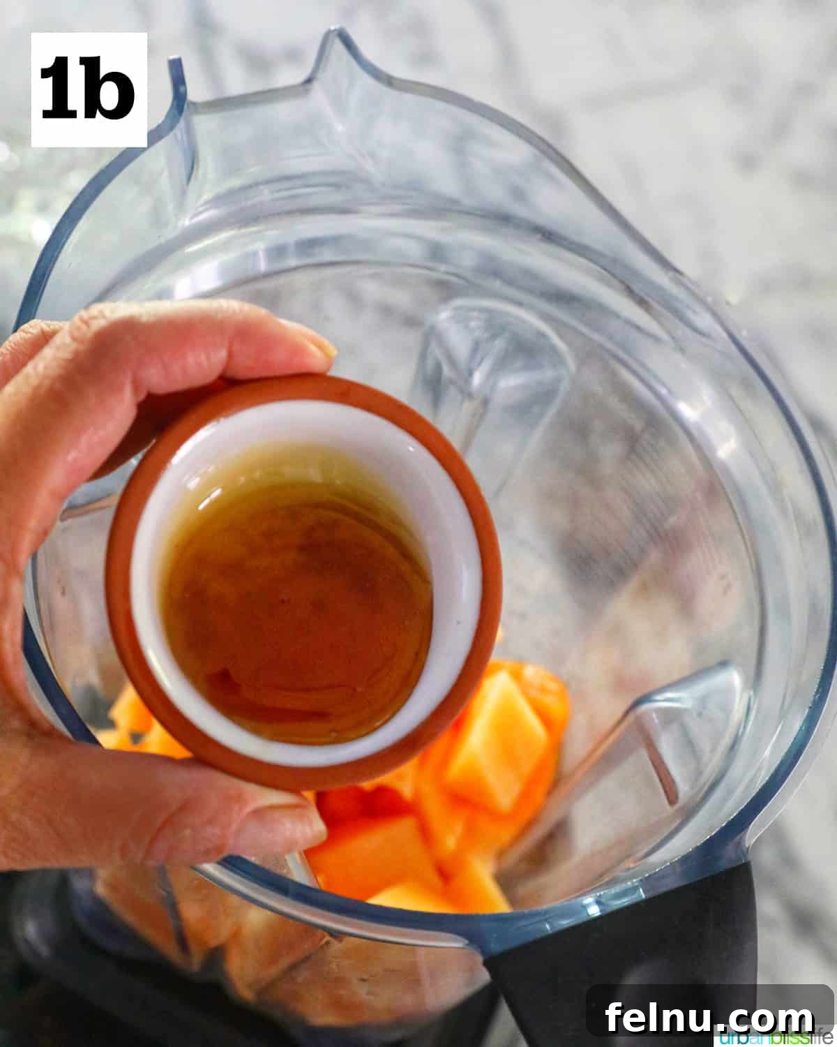 Hand adding agave nectar to a blender with chopped cantaloupe.