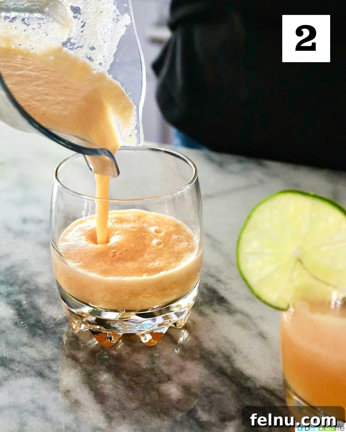Pouring melon margarita from a blender to a glass on a marble countertop.