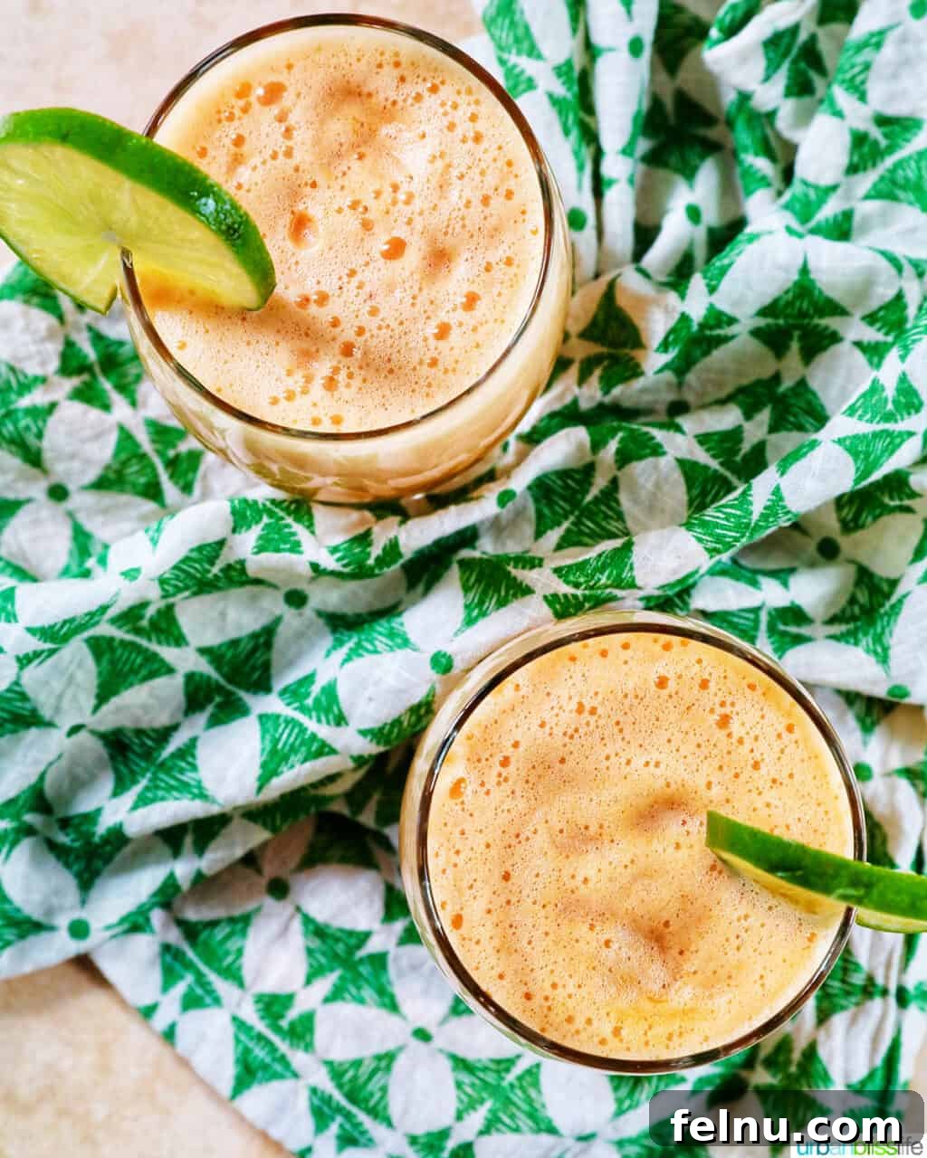 Two glasses of cantaloupe margaritas with lime slice garnish on a green and white patterned napkin.