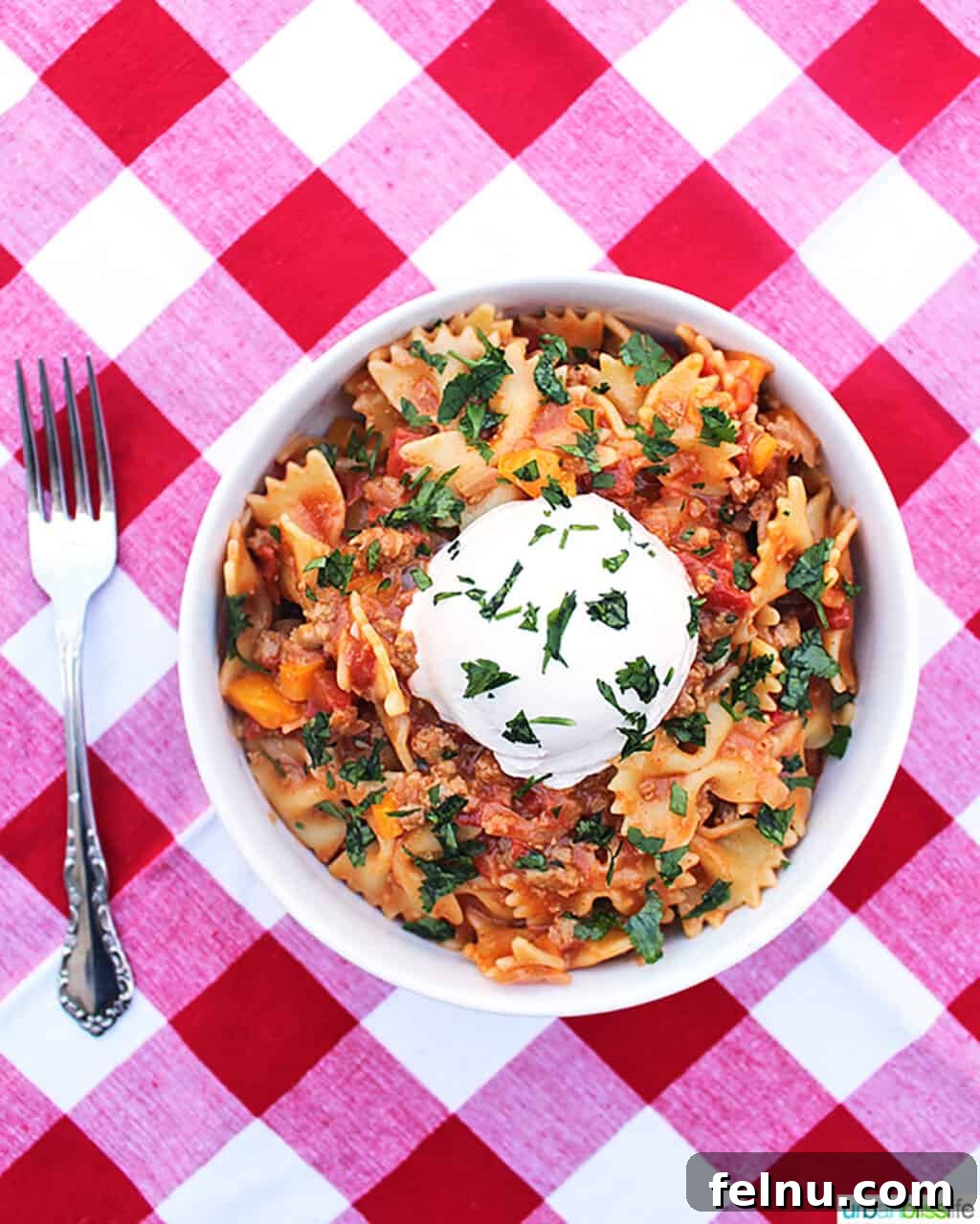 Taco Pasta served in a white bowl on a red and white checkered tablecloth, accompanied by a fork