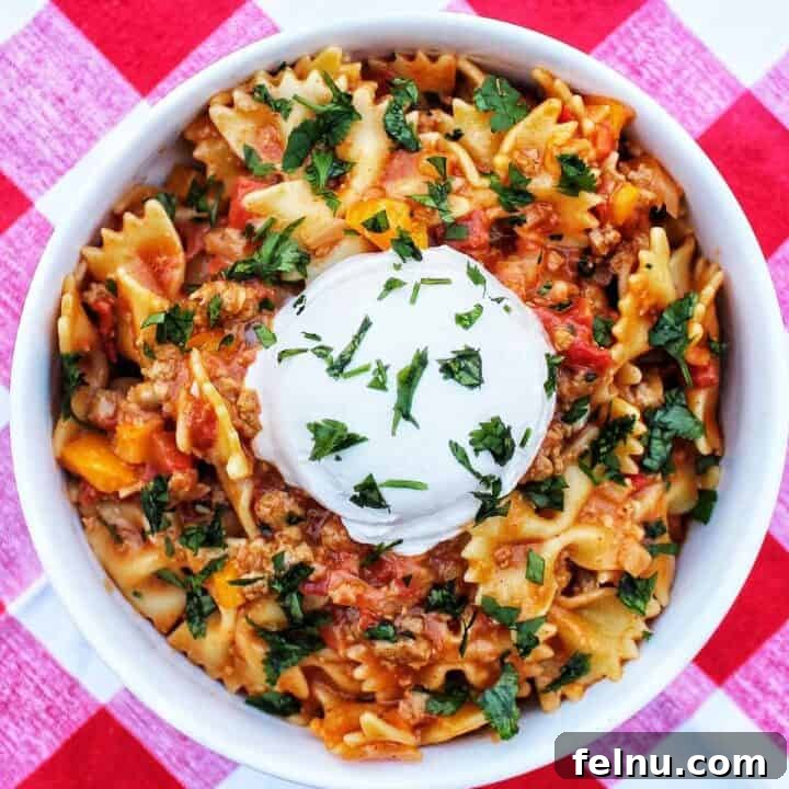 Taco Pasta with scoop of sour cream and chopped parsley on a red and white checkered tablecloth.
