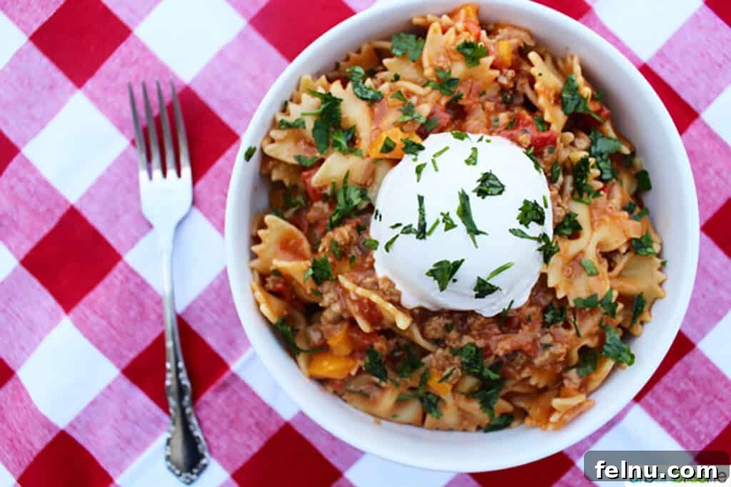 Cooked Taco Pasta served in a white bowl on a red and white checkered tablecloth.