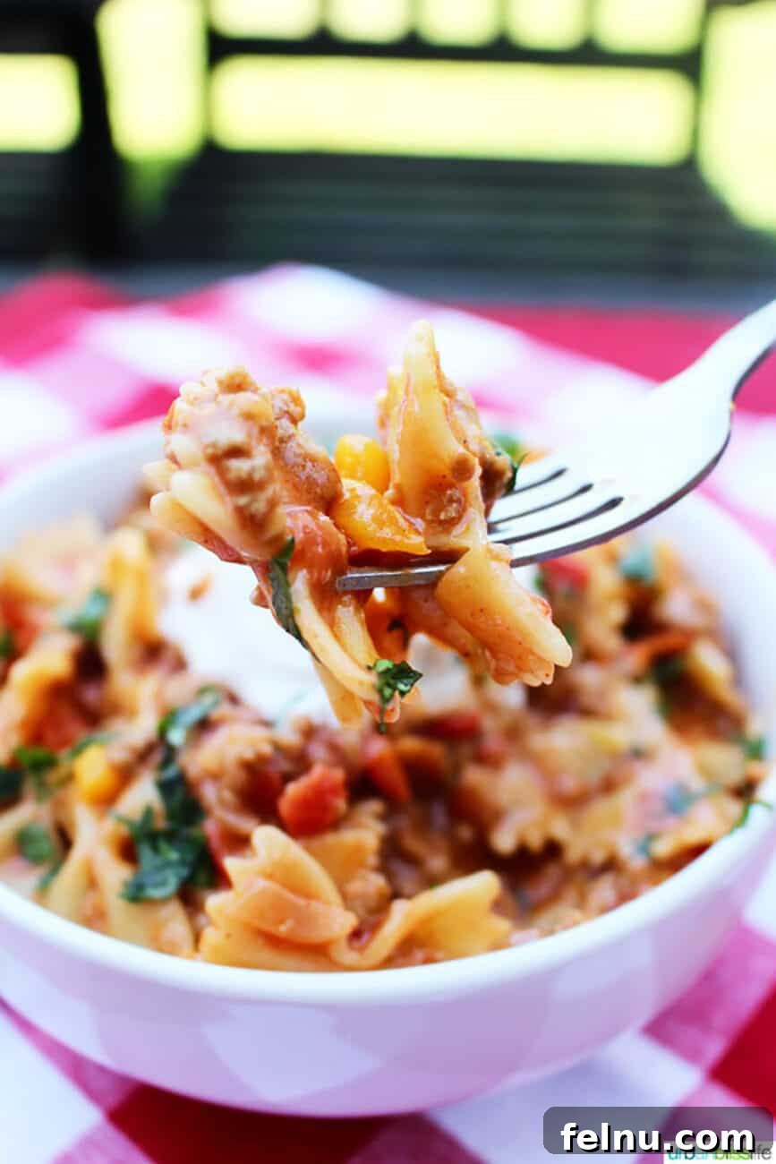 White bowl of Taco Pasta with toppings of sour cream, cheese, and cilantro