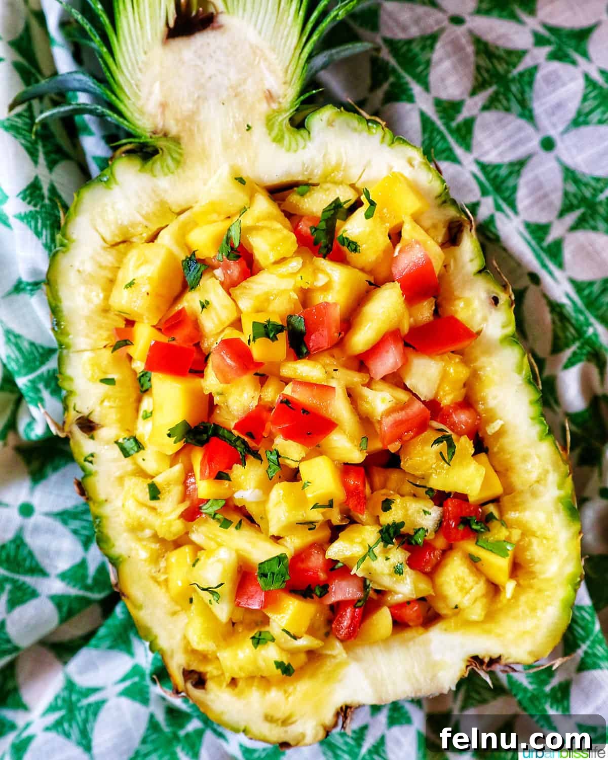 Sun-Kissed Fruit Salsa 3 A vibrant display of chopped pineapple, mango, tomatoes, and red onions in a hollowed-out pineapple shell, placed on a green patterned napkin, invitingly showcasing the fresh salsa.